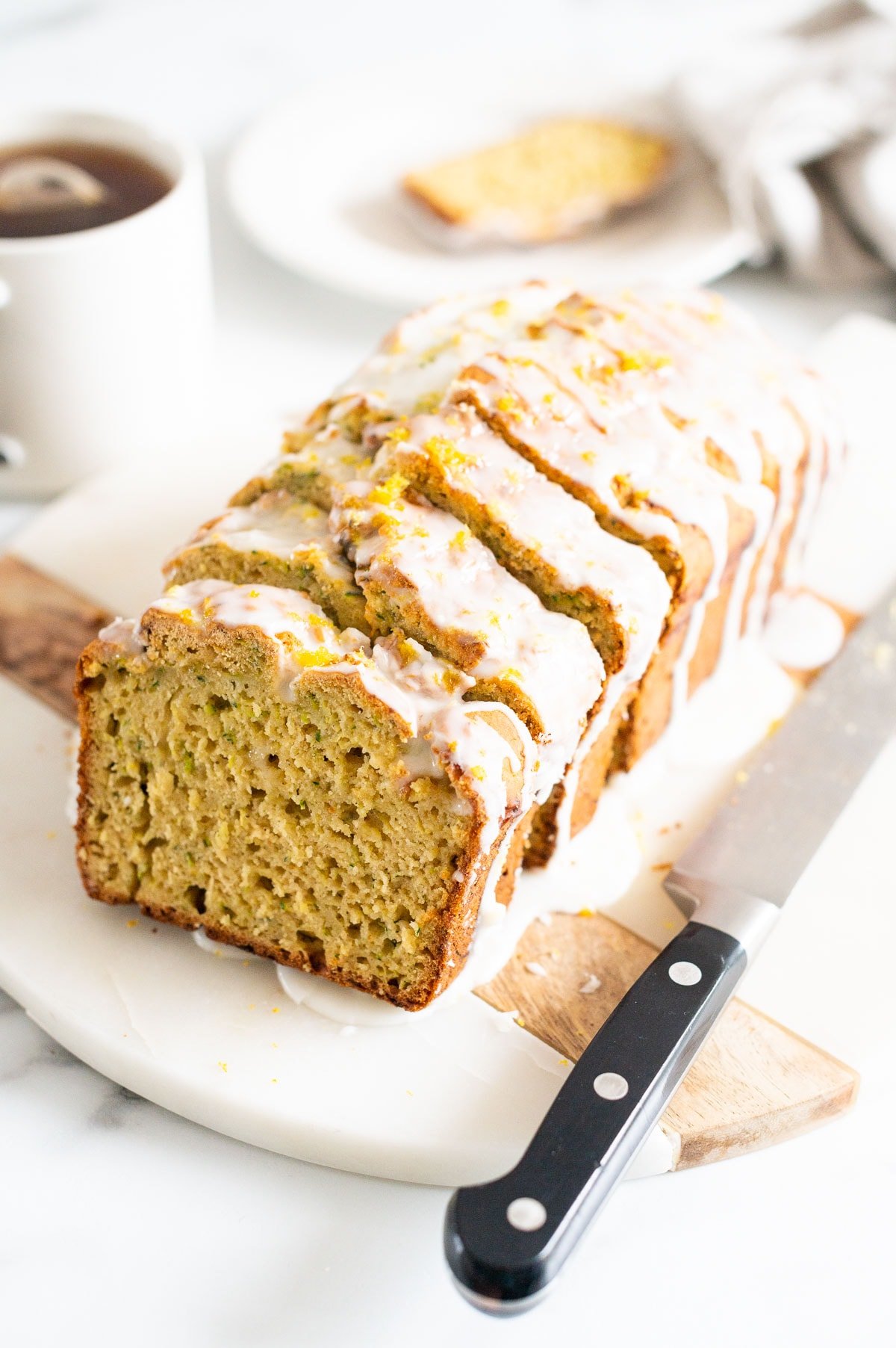 Sliced lemon zucchini bread on marble board with a knife.