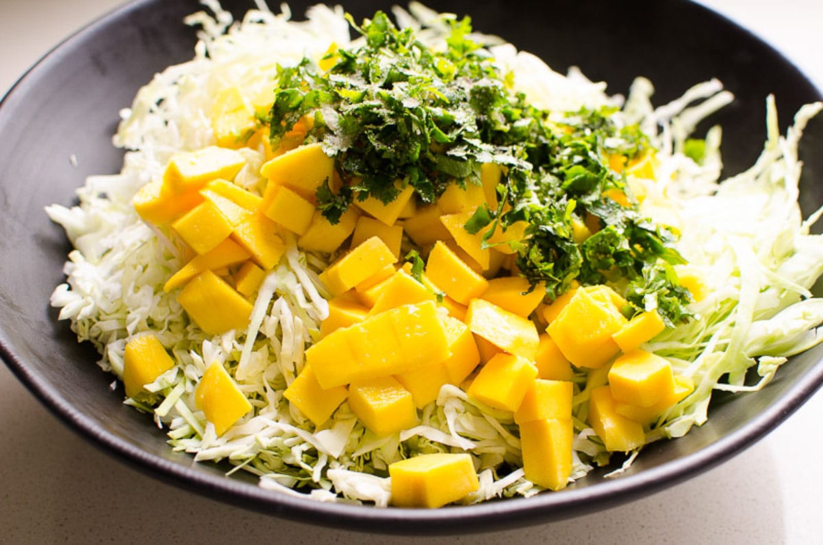 Shredded cabbage, diced mango and chopped cilantro in black bowl.
