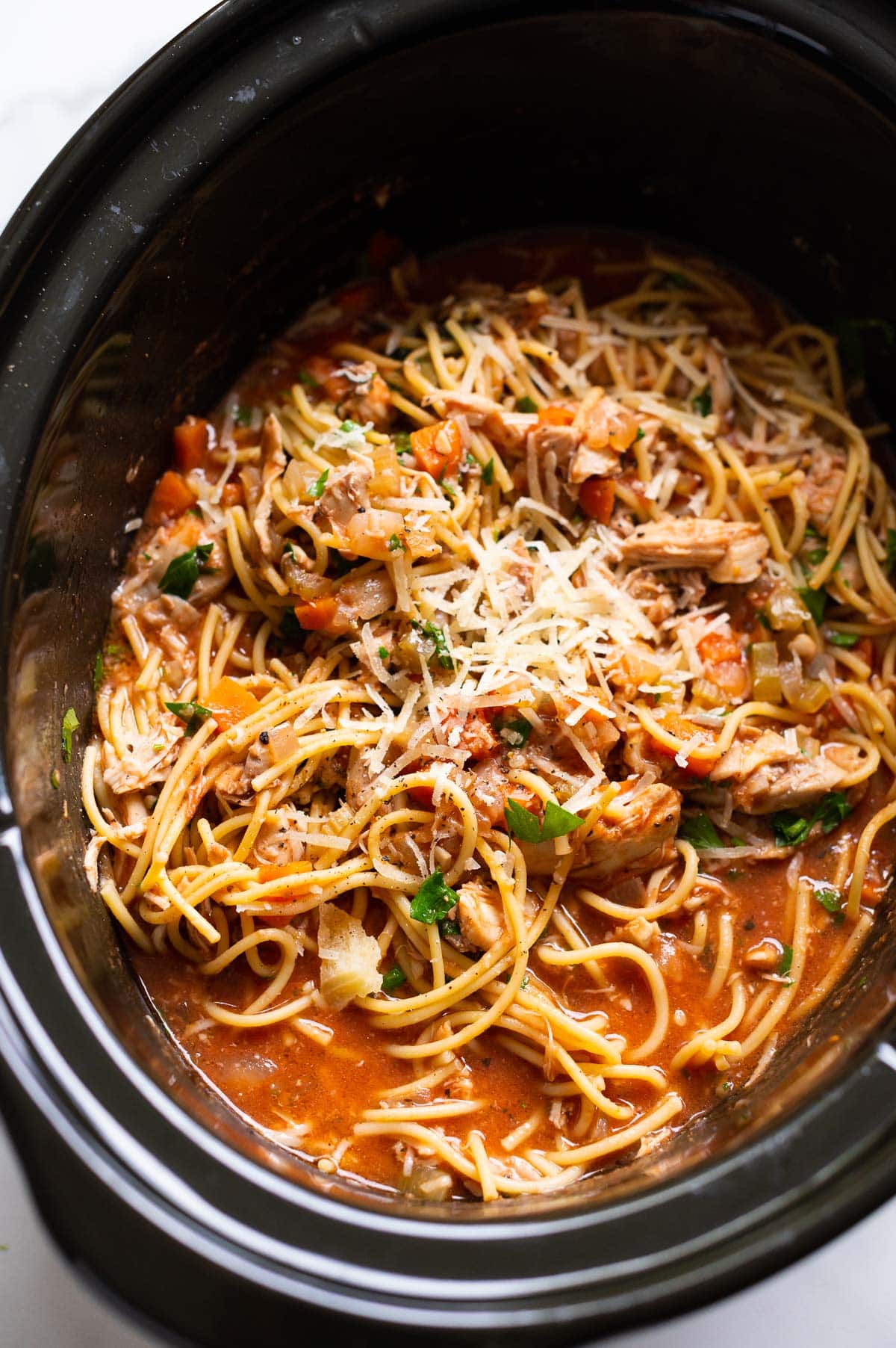 Side view of crockpot chicken spaghetti recipe in sauce inside slow cooker.