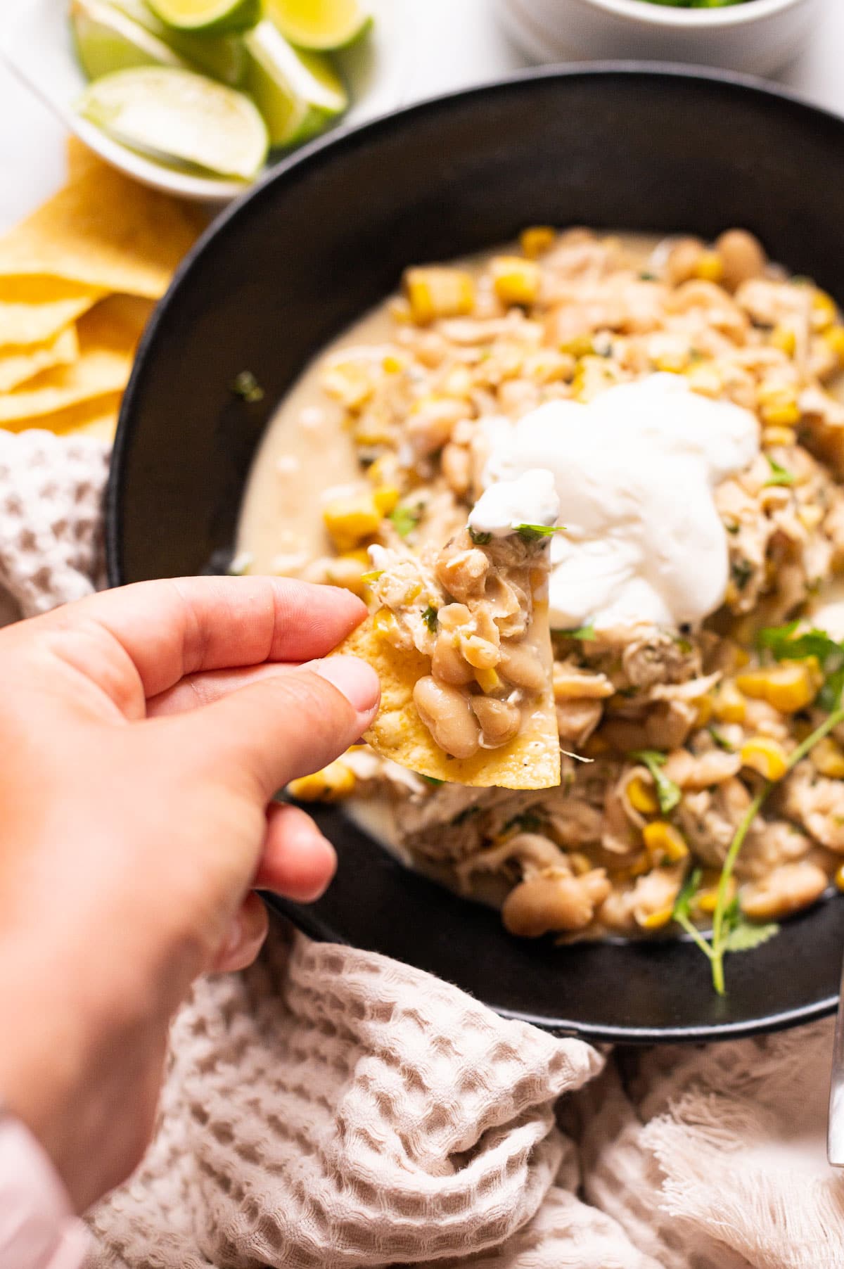 Person holding tortilla chip scooped into a bowl of slow cooker white chicken chili.