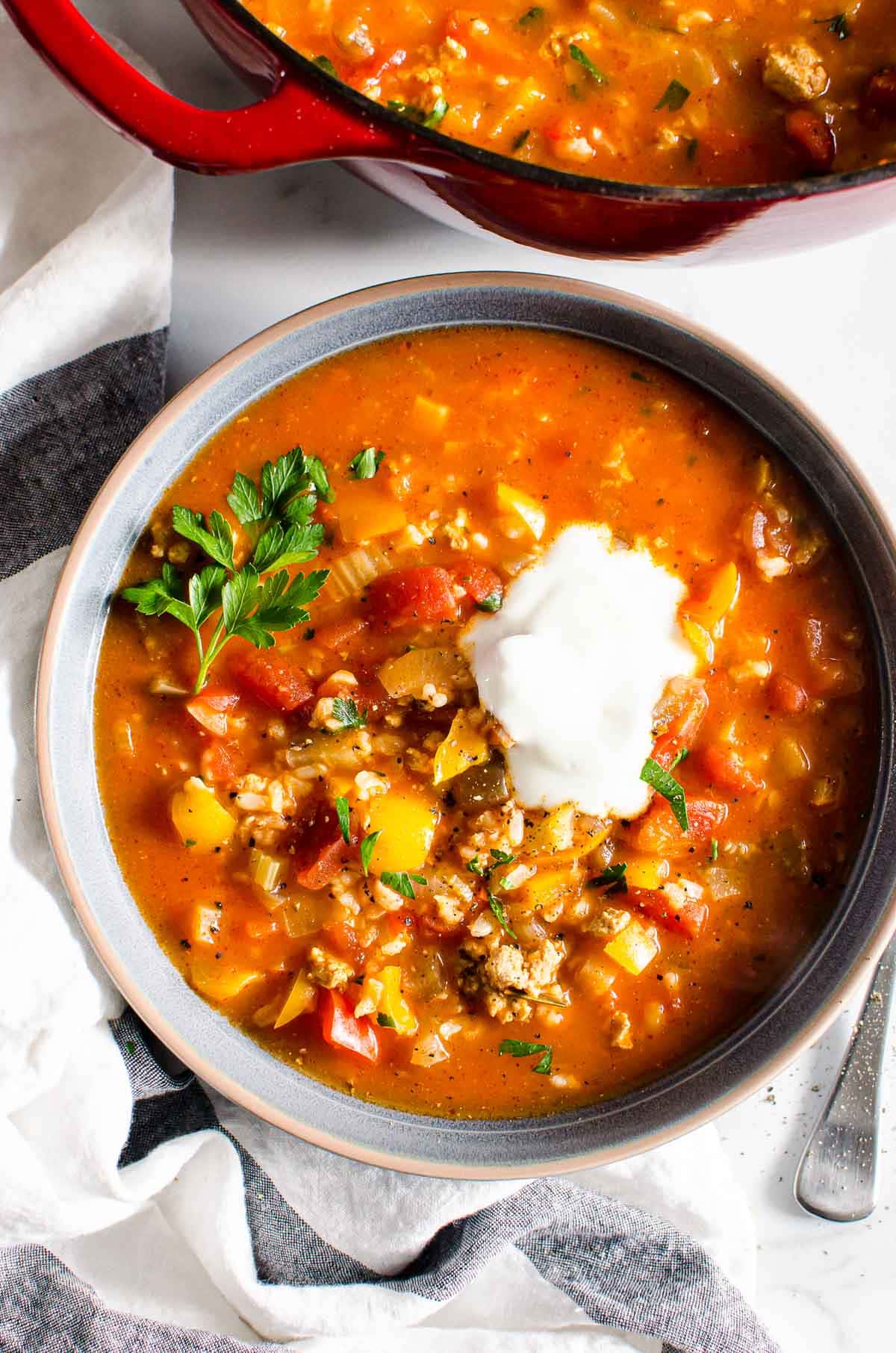 Stuffed bell pepper soup served in a bowl with dollop of sour cream and garnished with parsley.