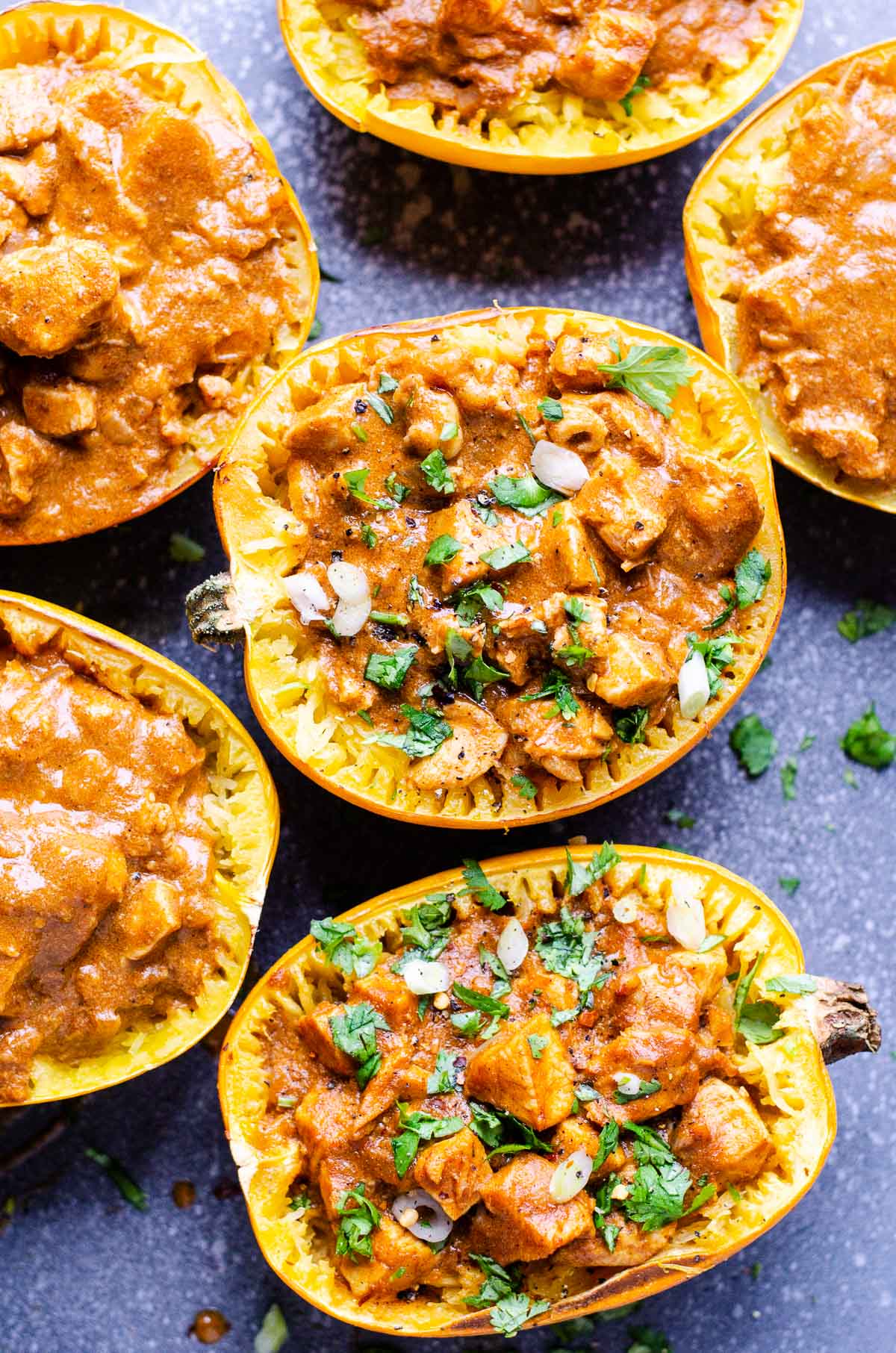 Six spaghetti squash halves with butter chicken sauce and garnished with cilantro and green onion.