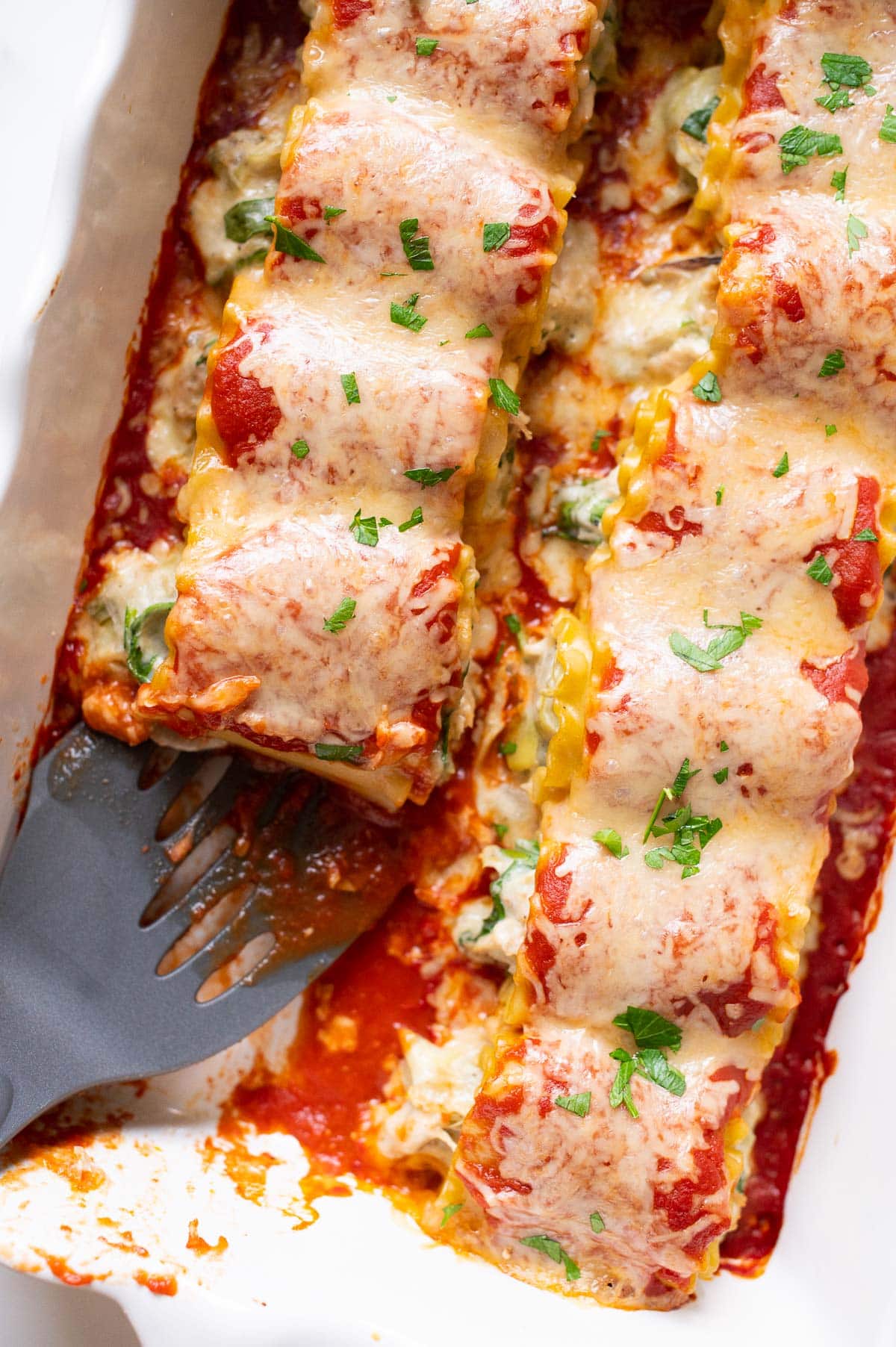 Chicken lasagna roll ups in a baking dish with one missing and spatula in it.