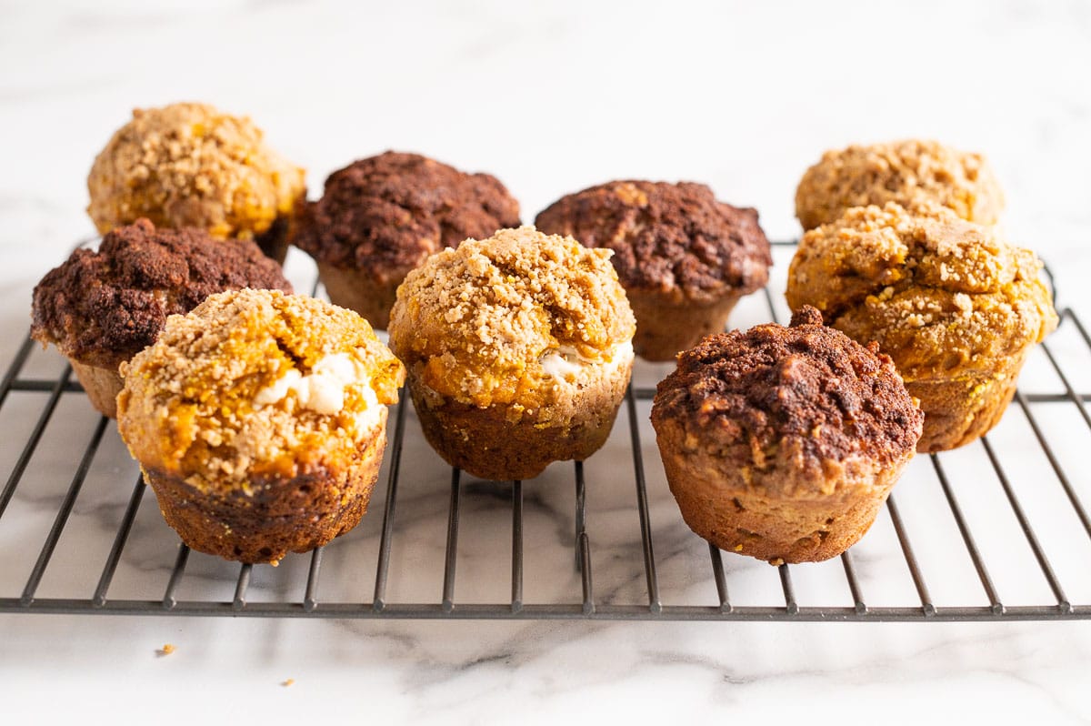 Apple cinnamon muffins and pumpkin cream cheese muffins cooling off on a wire rack.