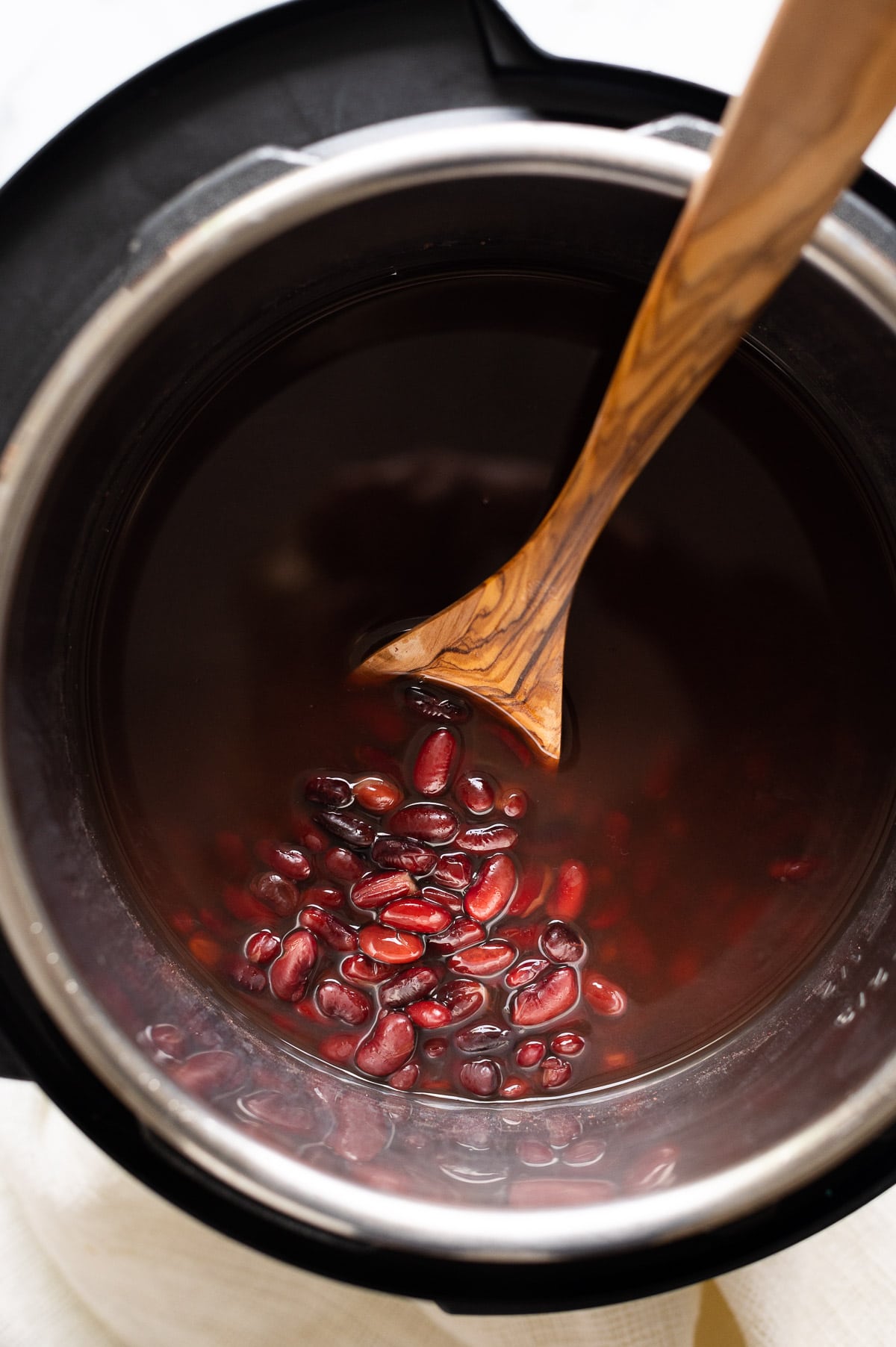 Instant Pot kidney beans in liquid in the pot with a spoon.