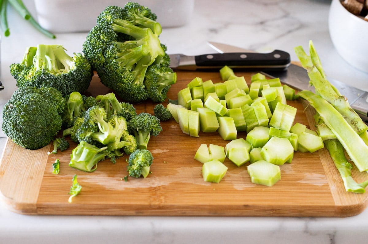Broccoli crowns, and peeled and chopped broccoli stalks on a cutting board with knives.