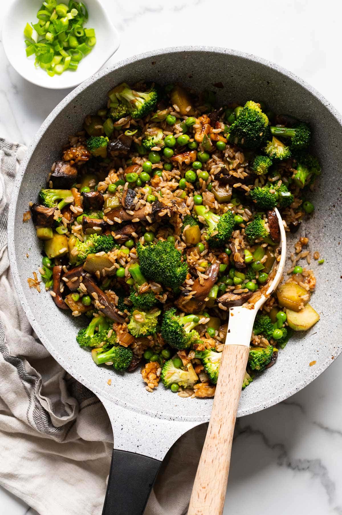Broccoli mushroom stir fry with peas and brown rice in a skillet with a spoon.
