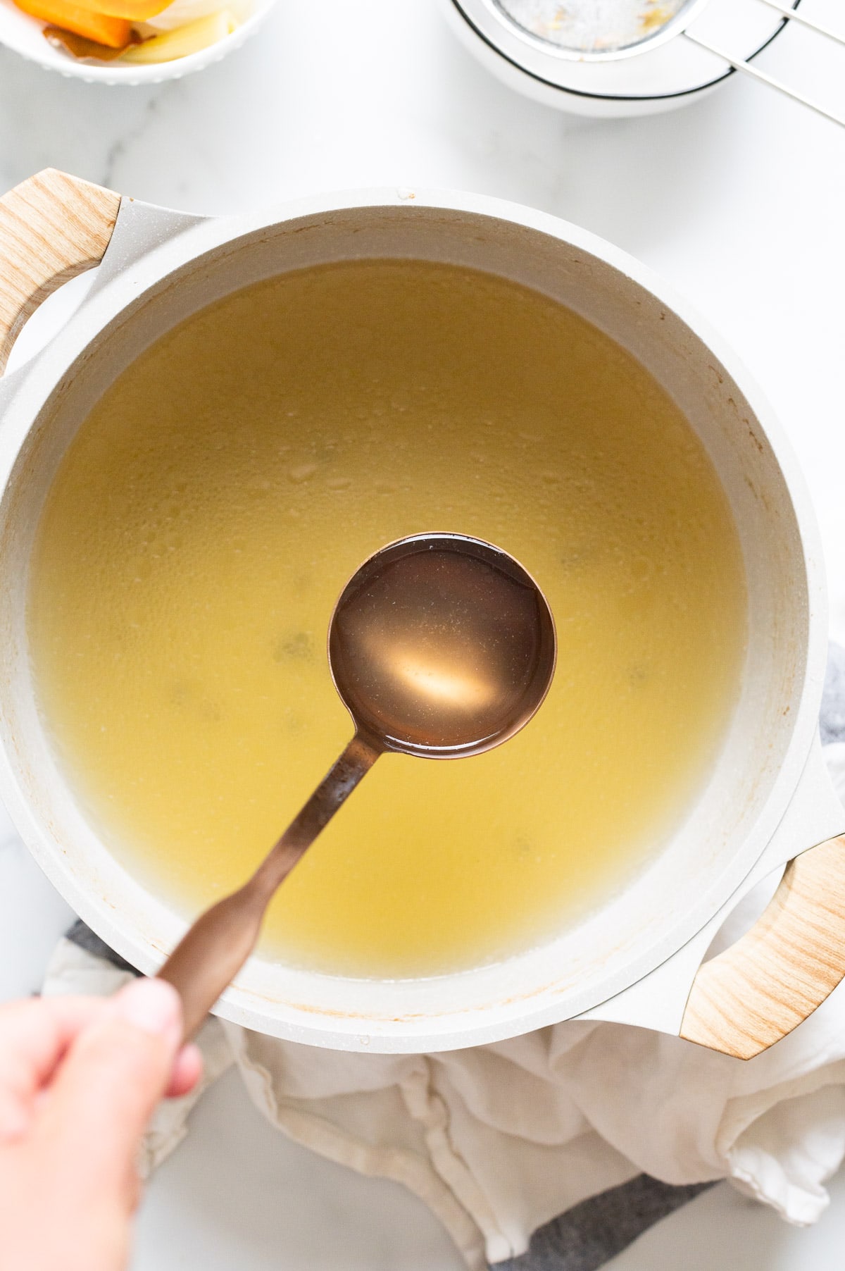 Person holding a ladle full of chicken broth above the pot with more broth.
