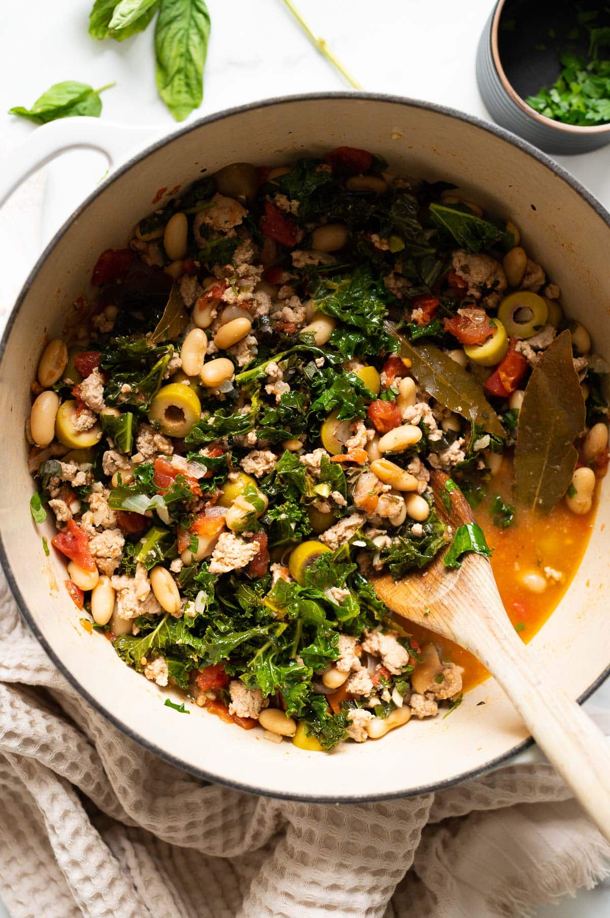 Ground Turkey Stew with kale, beans and olives in white pot.