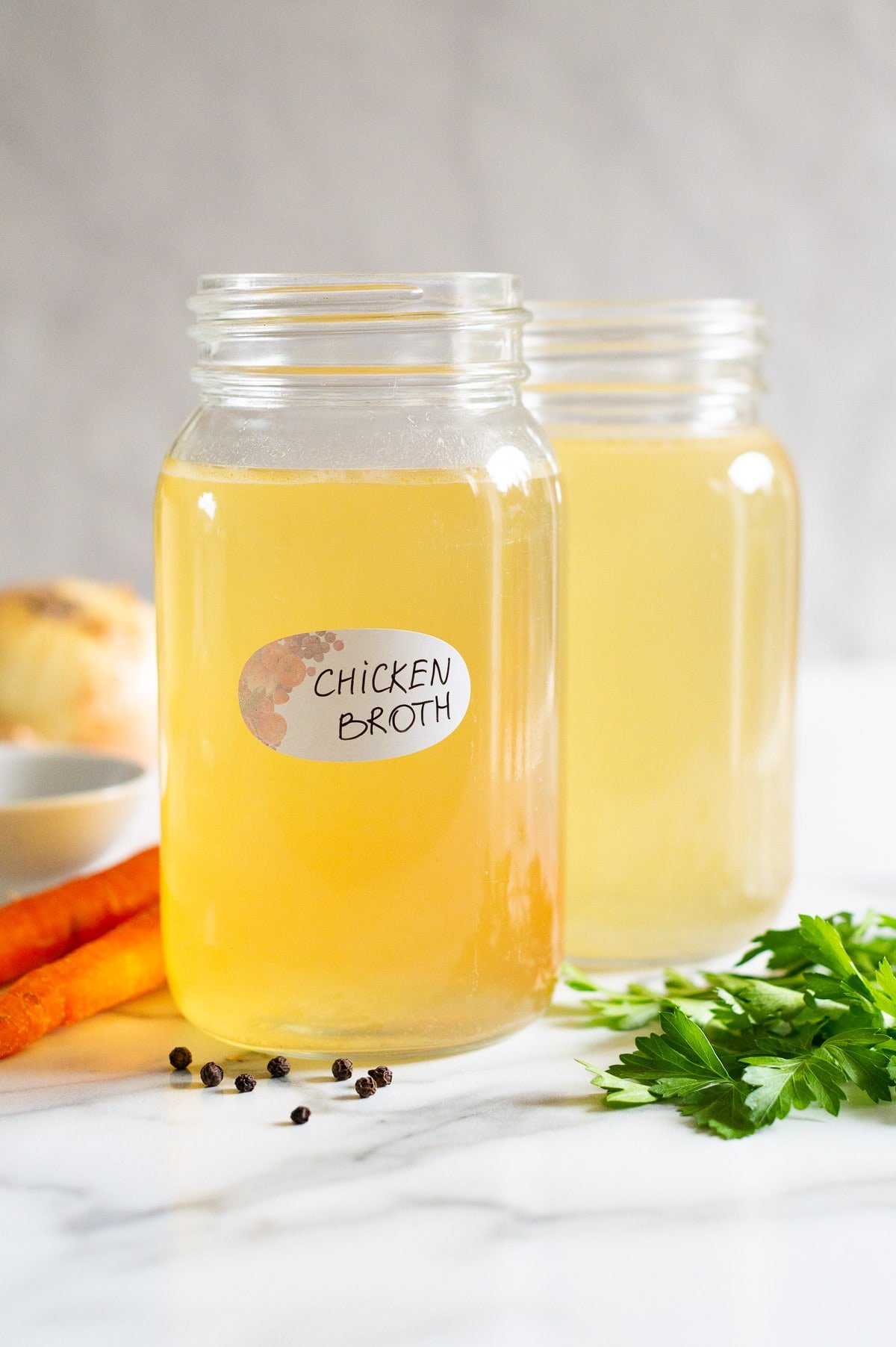 Chicken broth in glass jars with vegetables on a counter.