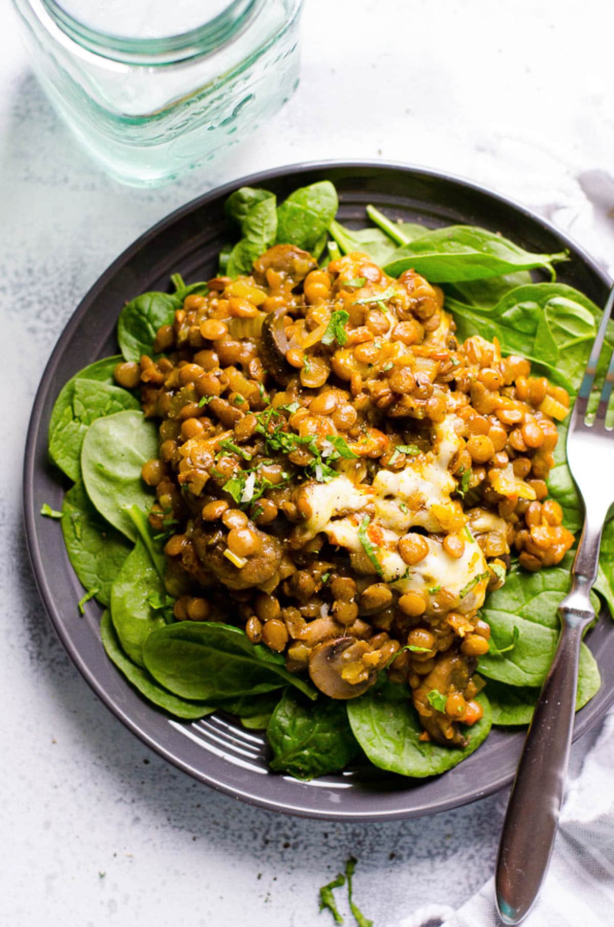 Lentil casserole served on a bed of baby spinach on a plate with a fork.