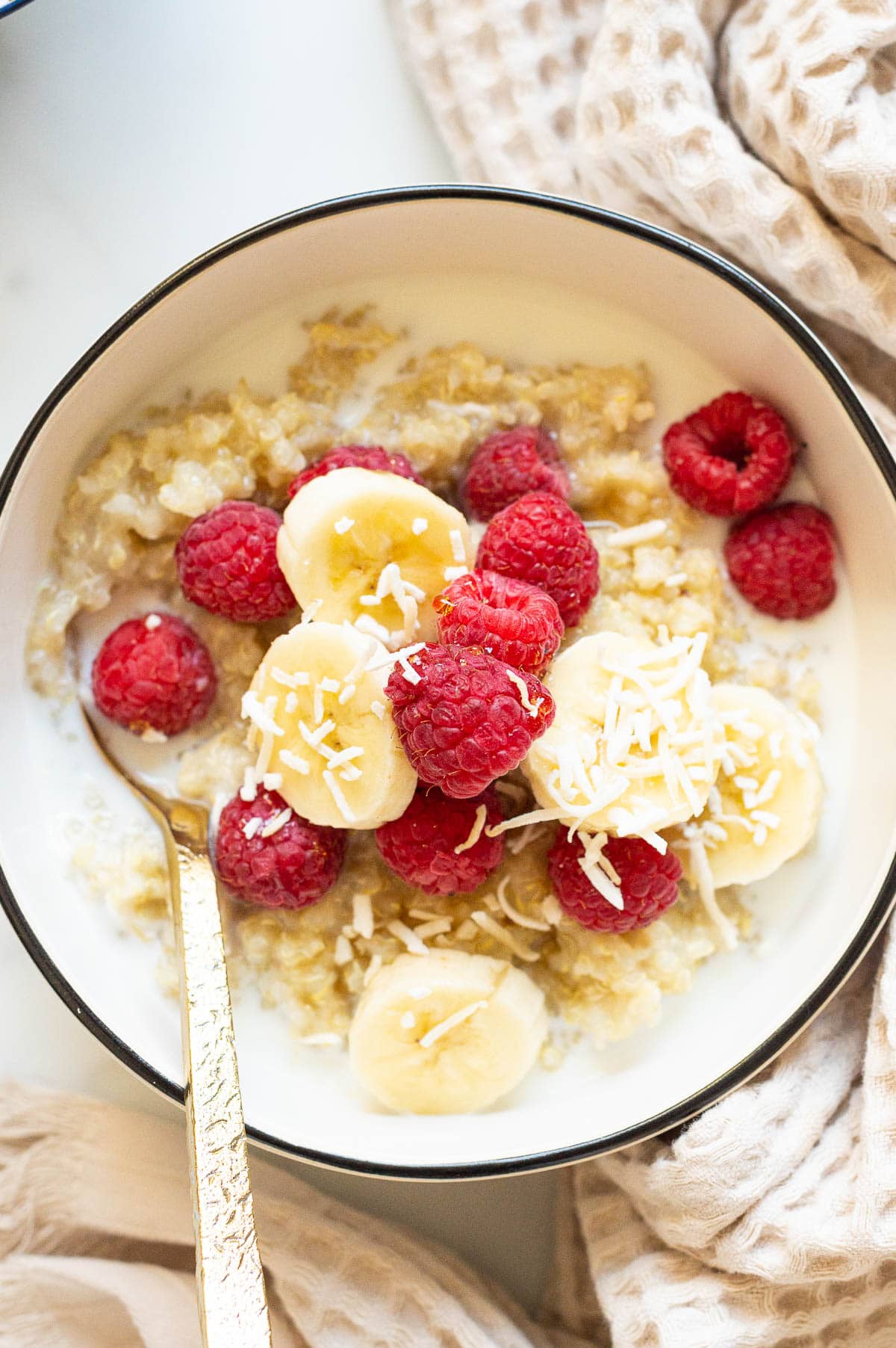 Quinoa breakfast bowl with milk, raspberries, banana and coconut flakes.