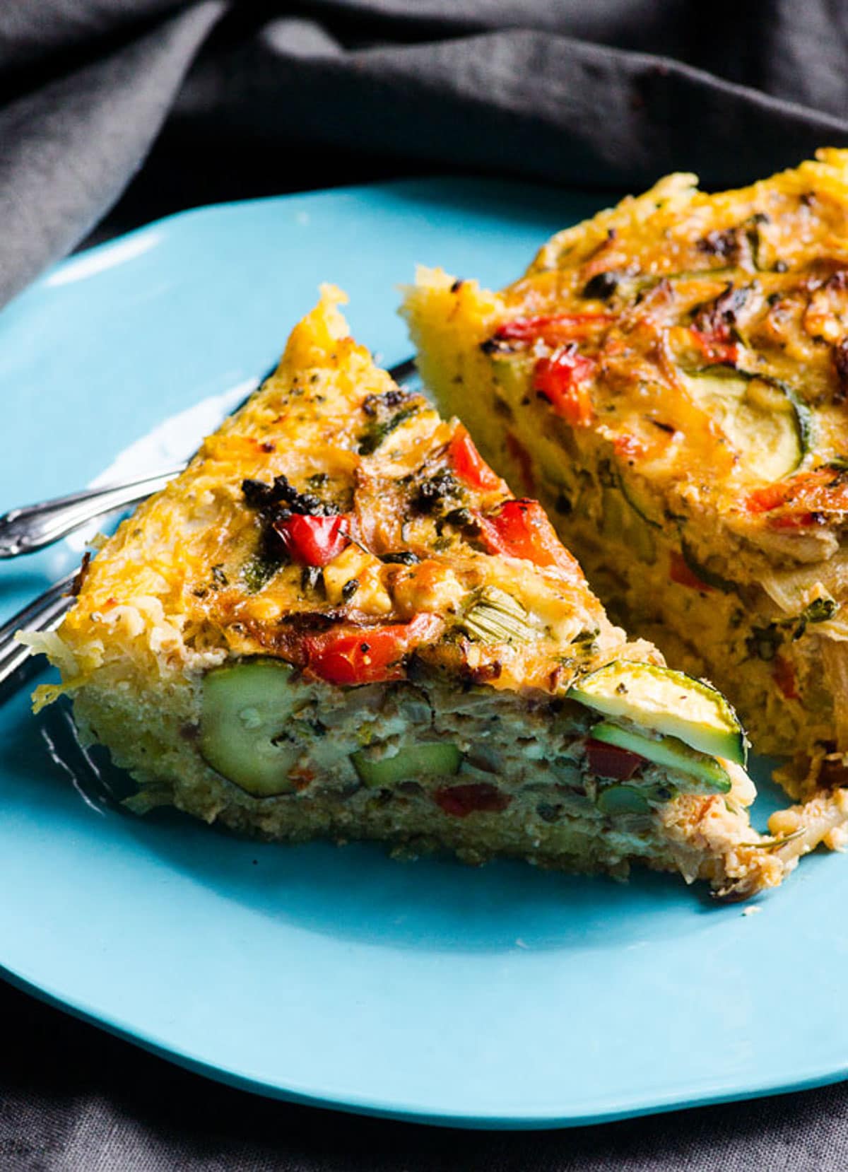 Two slices of spaghetti squash pie on blue plate with utensils.