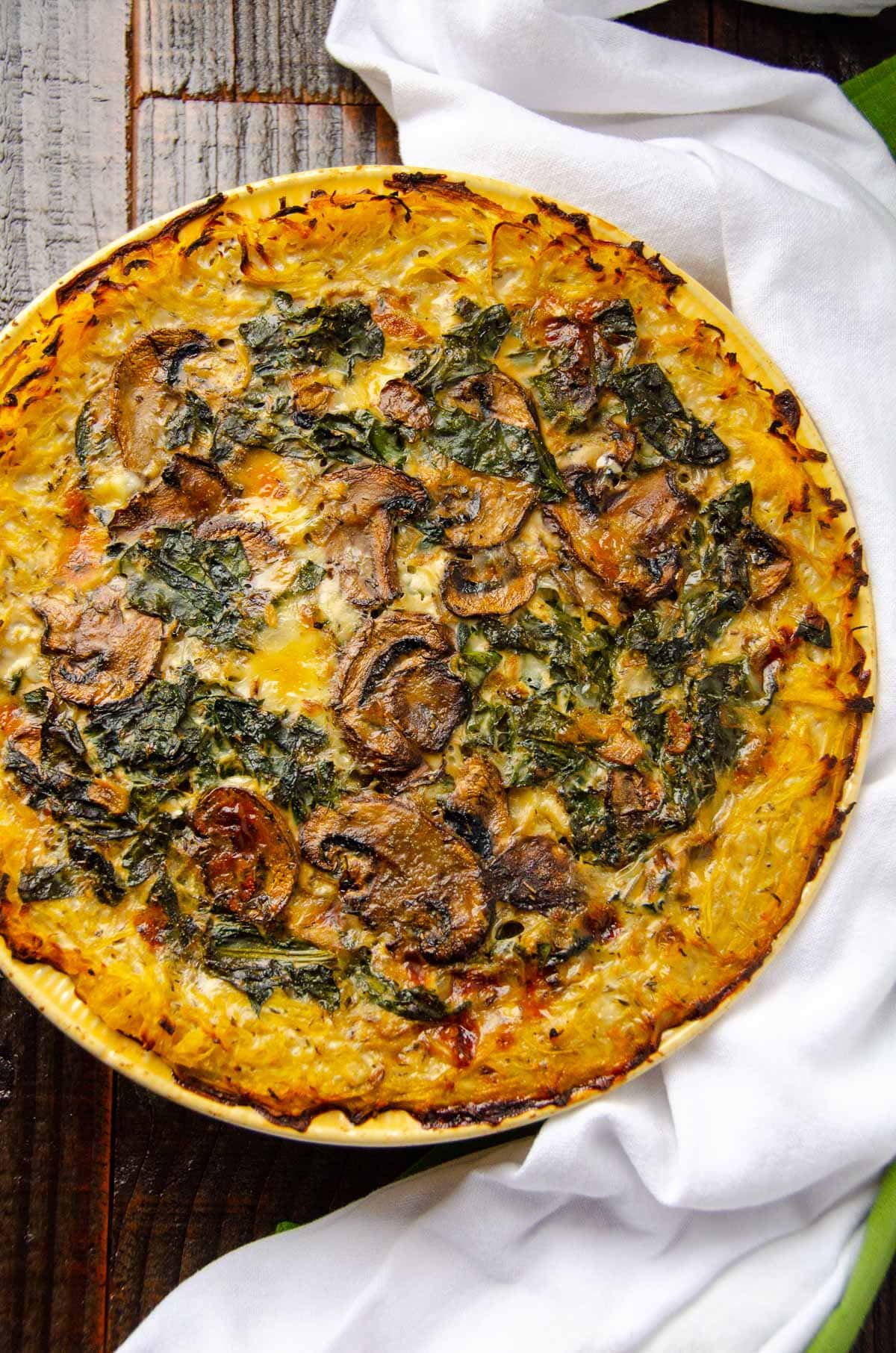 Looking down on baked spaghetti squash quiche with kale and mushrooms in a pie dish.