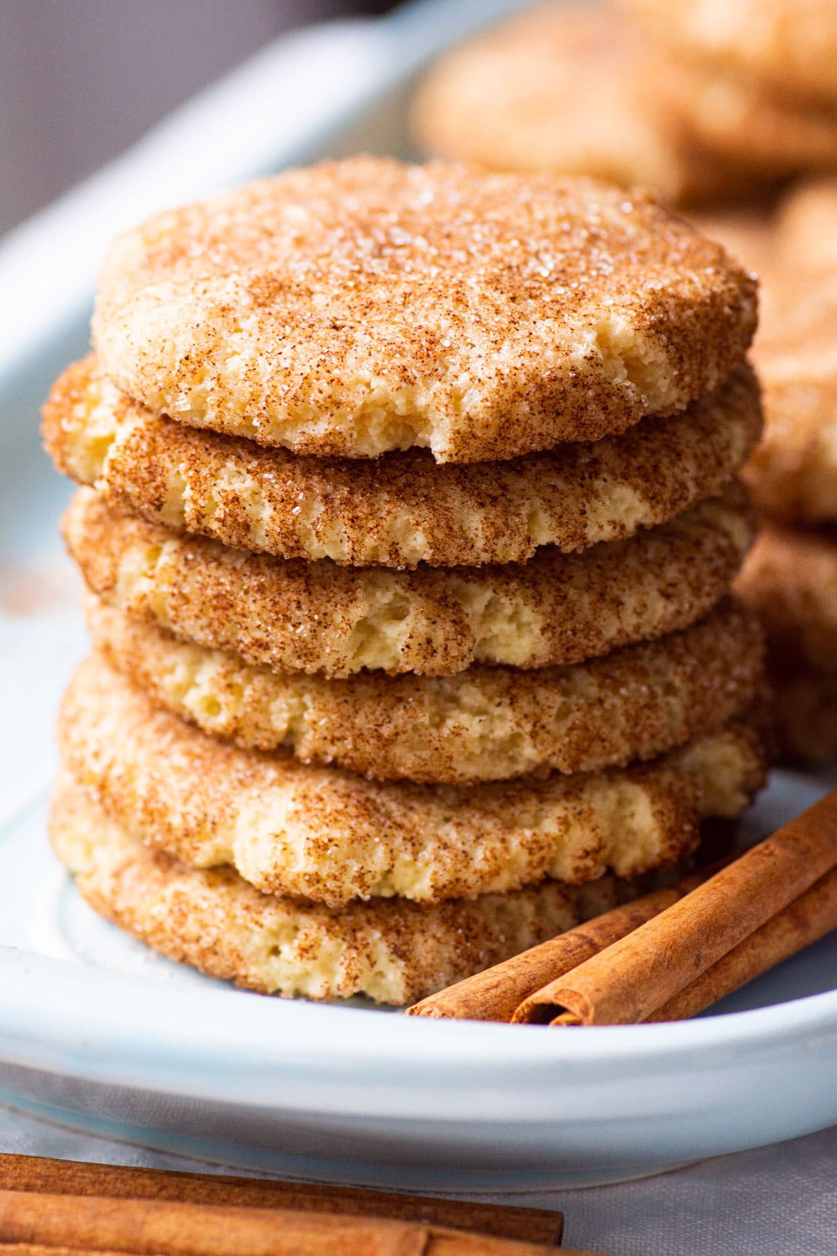 Almond flour snickerdoodles stacked on a plate with cinnamon sticks.