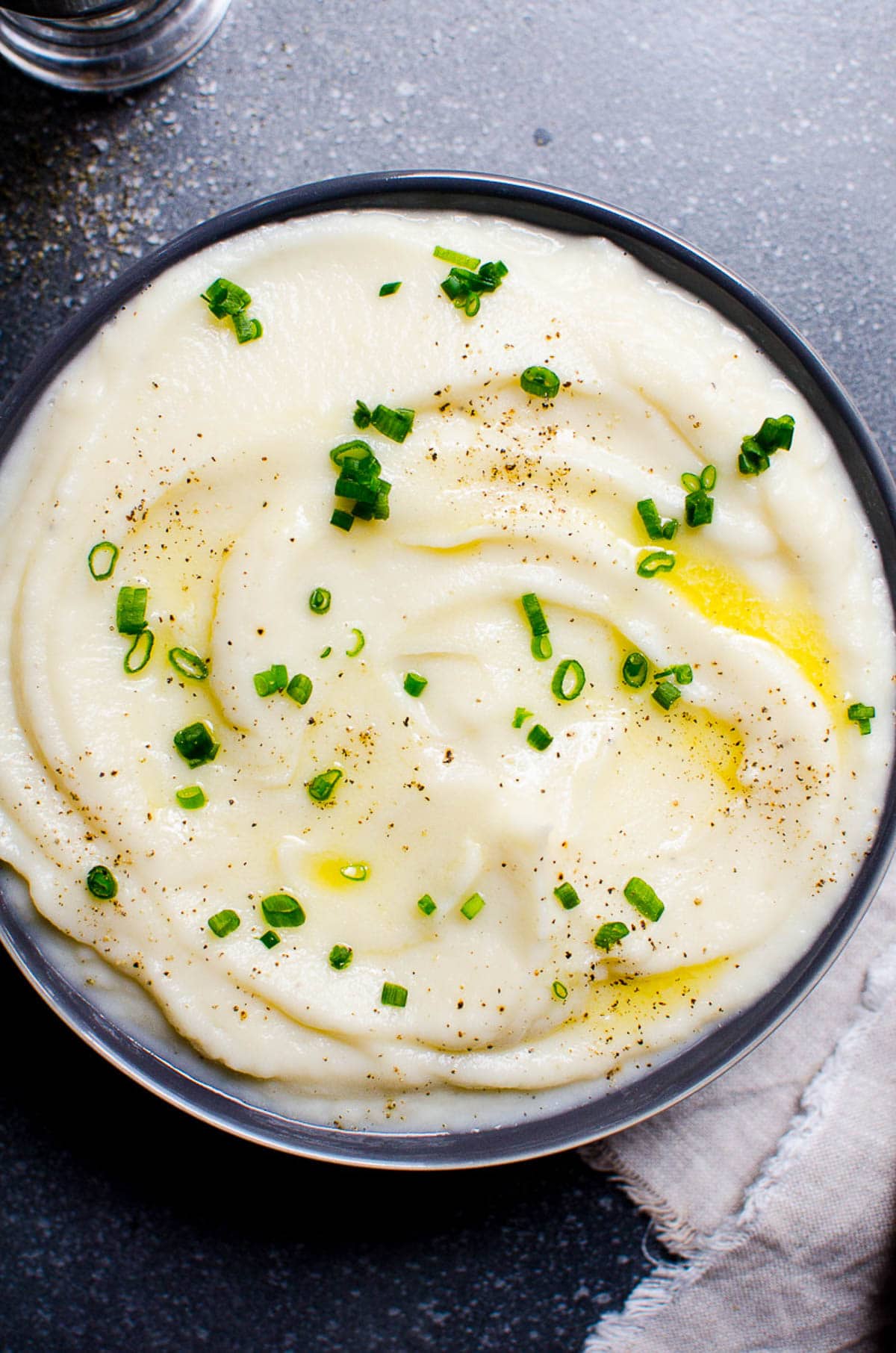 Mashed cauliflower served in a bowl garnished with melted butter, chives and pepper.
