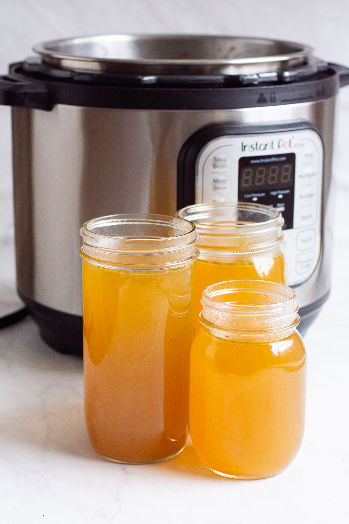 Instant Pot chicken broth in three glass jars with Instant Pot in the background.