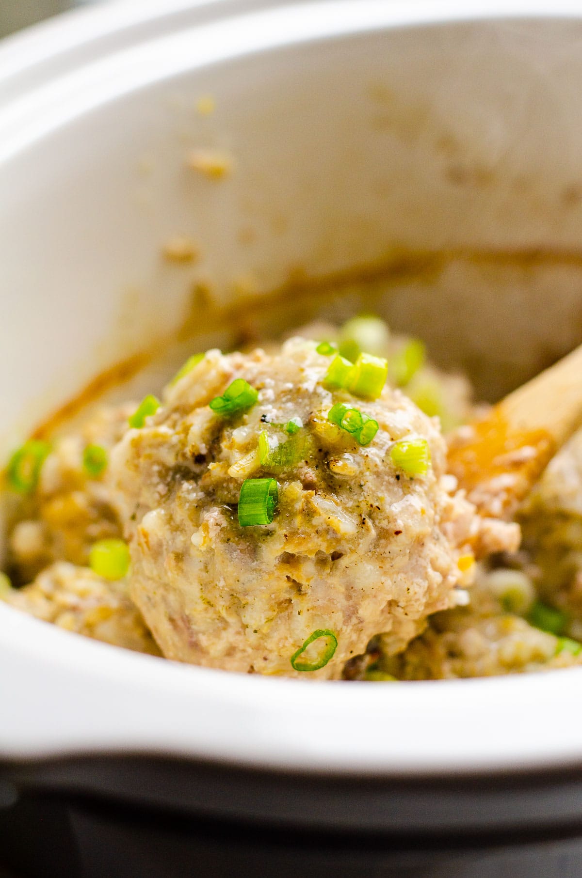 Porcupine meatball garnished with green onion on a spoon.