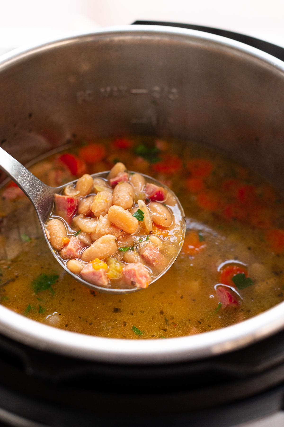 Ham and bean soup on a ladle above the pot.