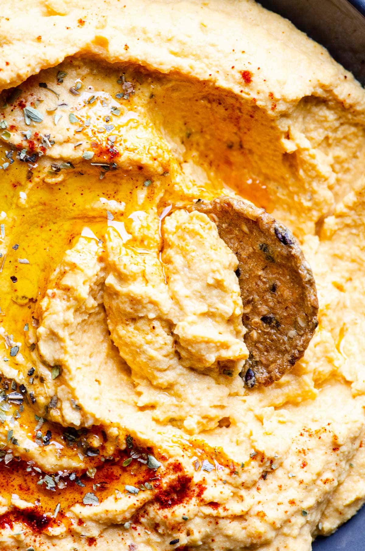Close up of sweet potato hummus drizzled with olive oil and sprinkled with spices and cracker in it.