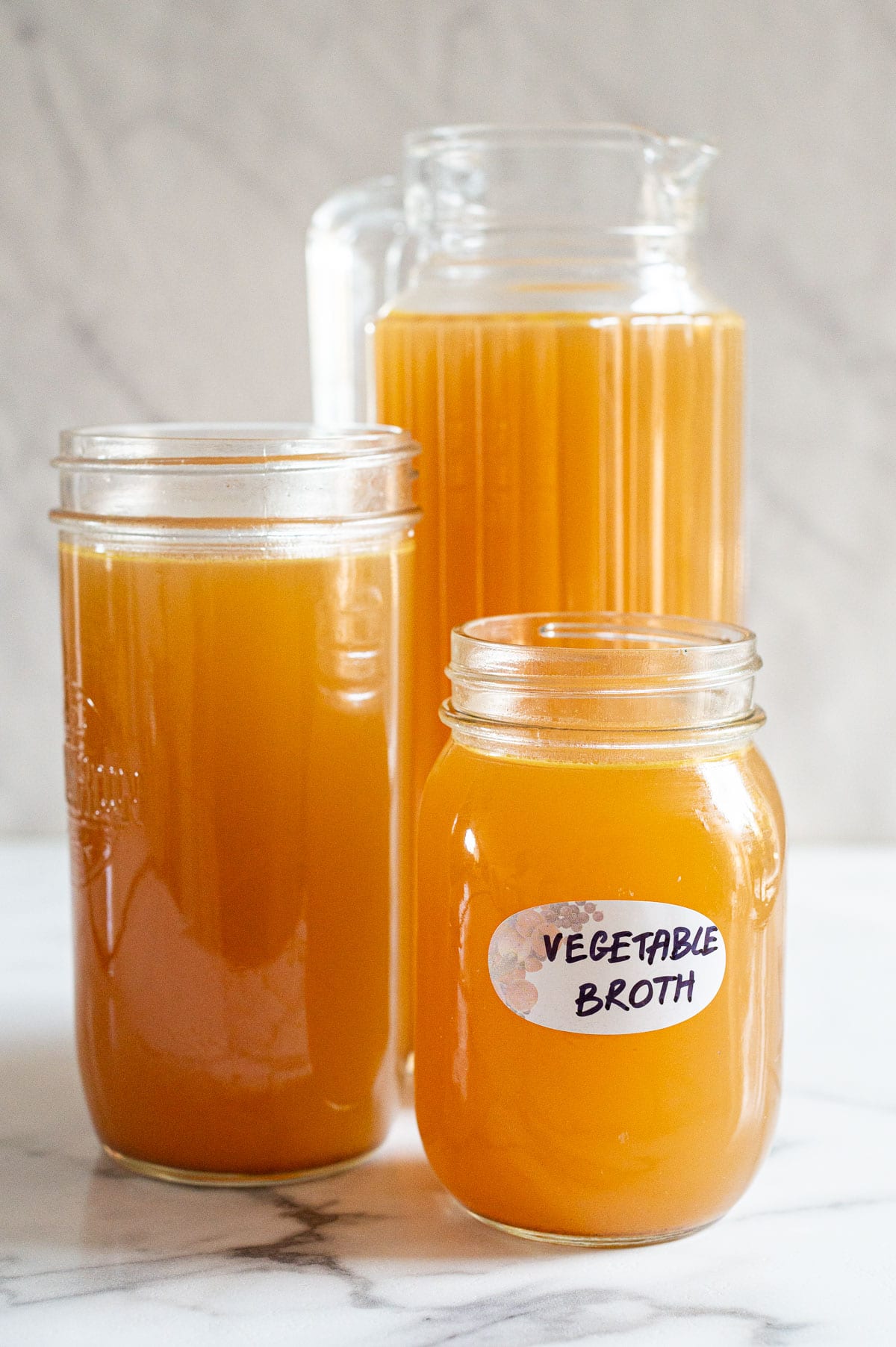Homemade vegetable broth in three glass jars and one of them labeled.