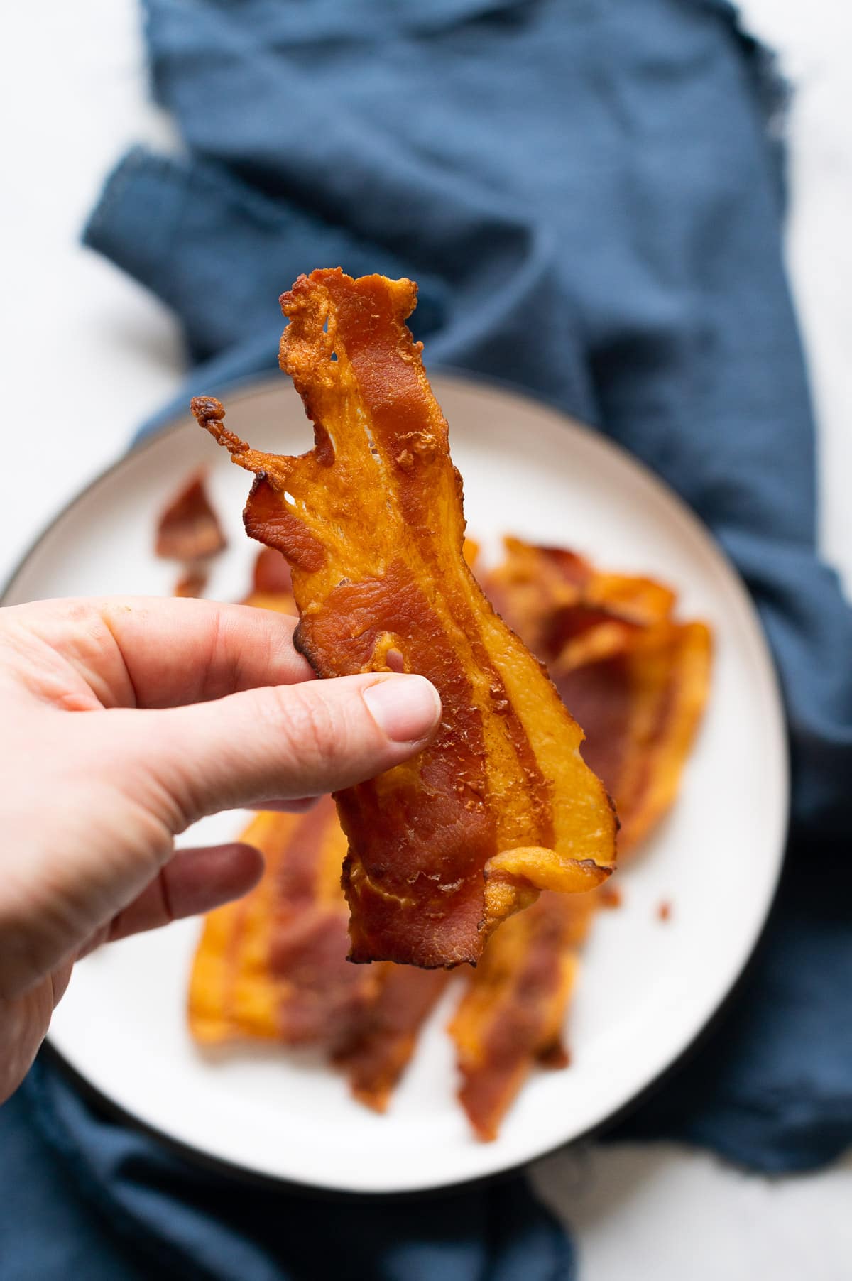 Person holding crispy baked bacon slice.