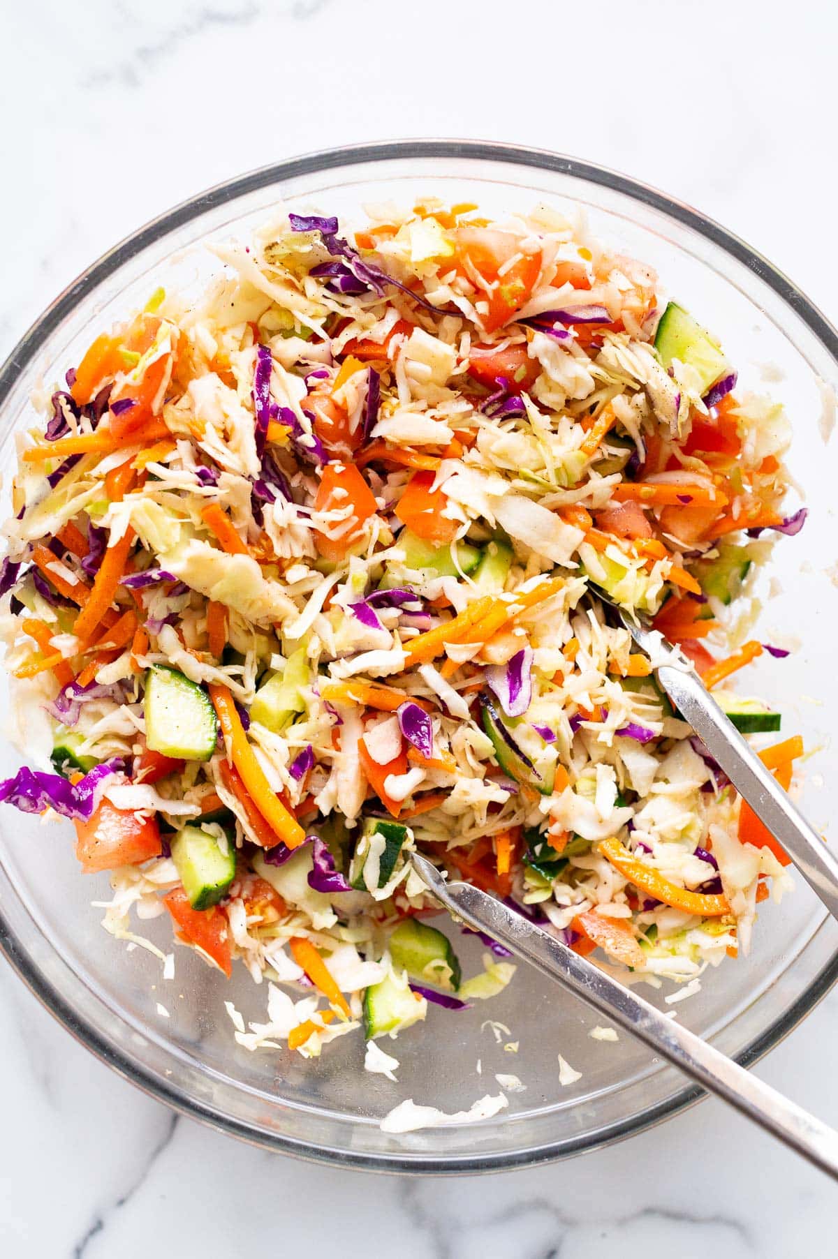 Coleslaw in a glass bowl with metal tongs.
