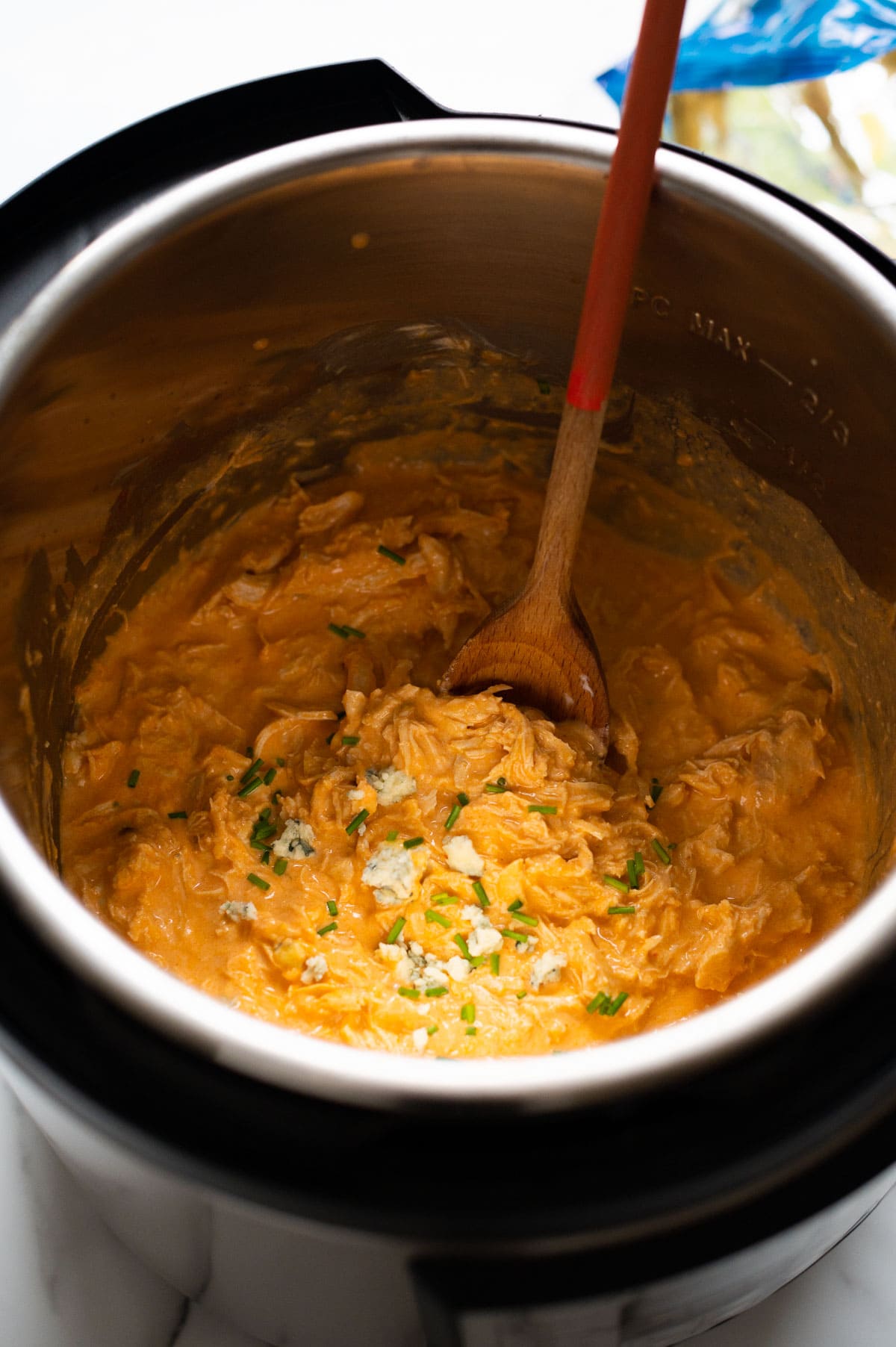 Buffalo chicken dip in instant pot garnished with chives and blue cheese and wooden spoon in it.