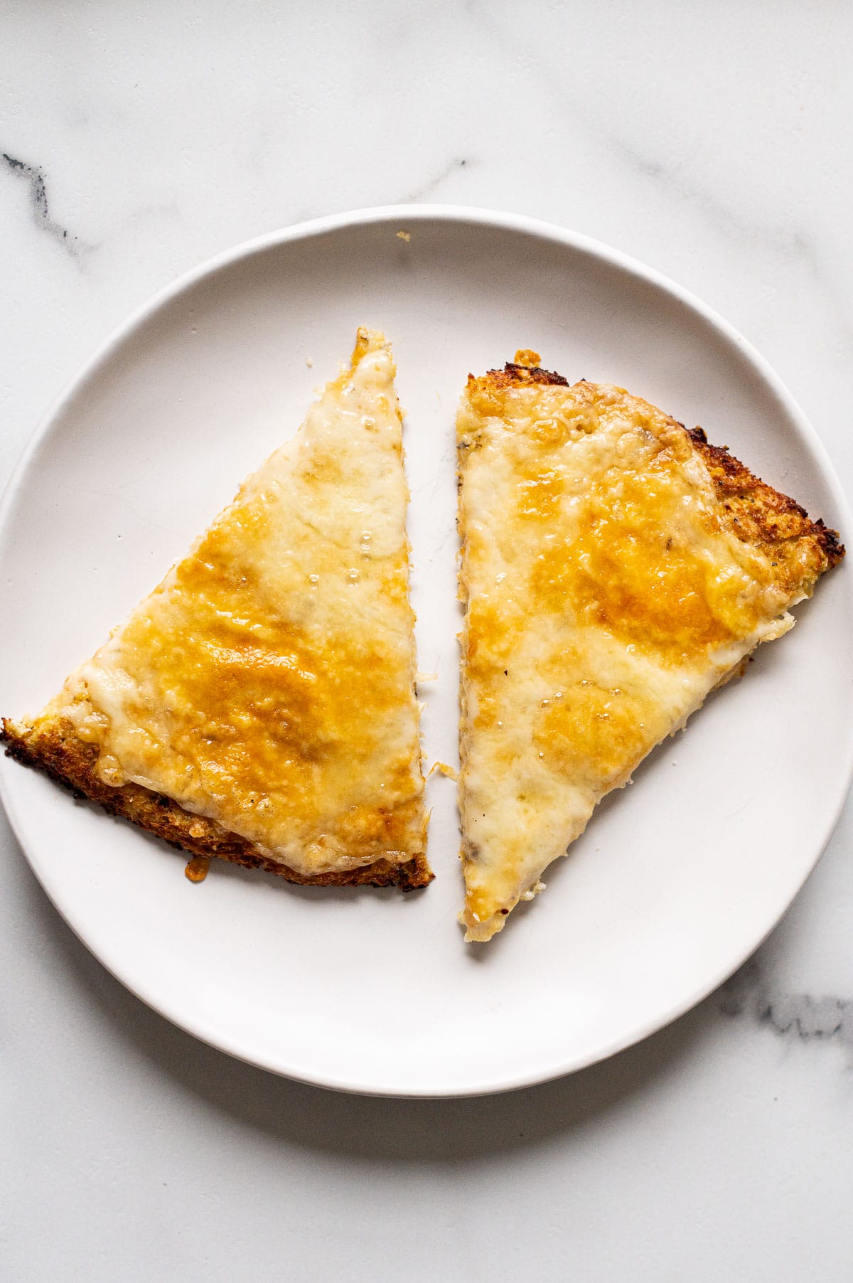 Two cheese cauliflower pizza crust slices on white plate.