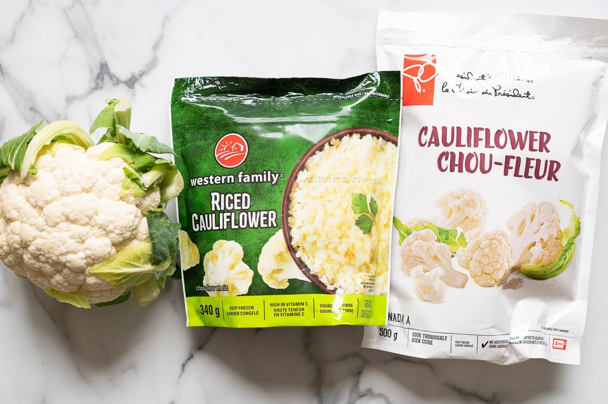 Head of cauliflower, cauliflower rice and frozen cauliflower florets in a bag.