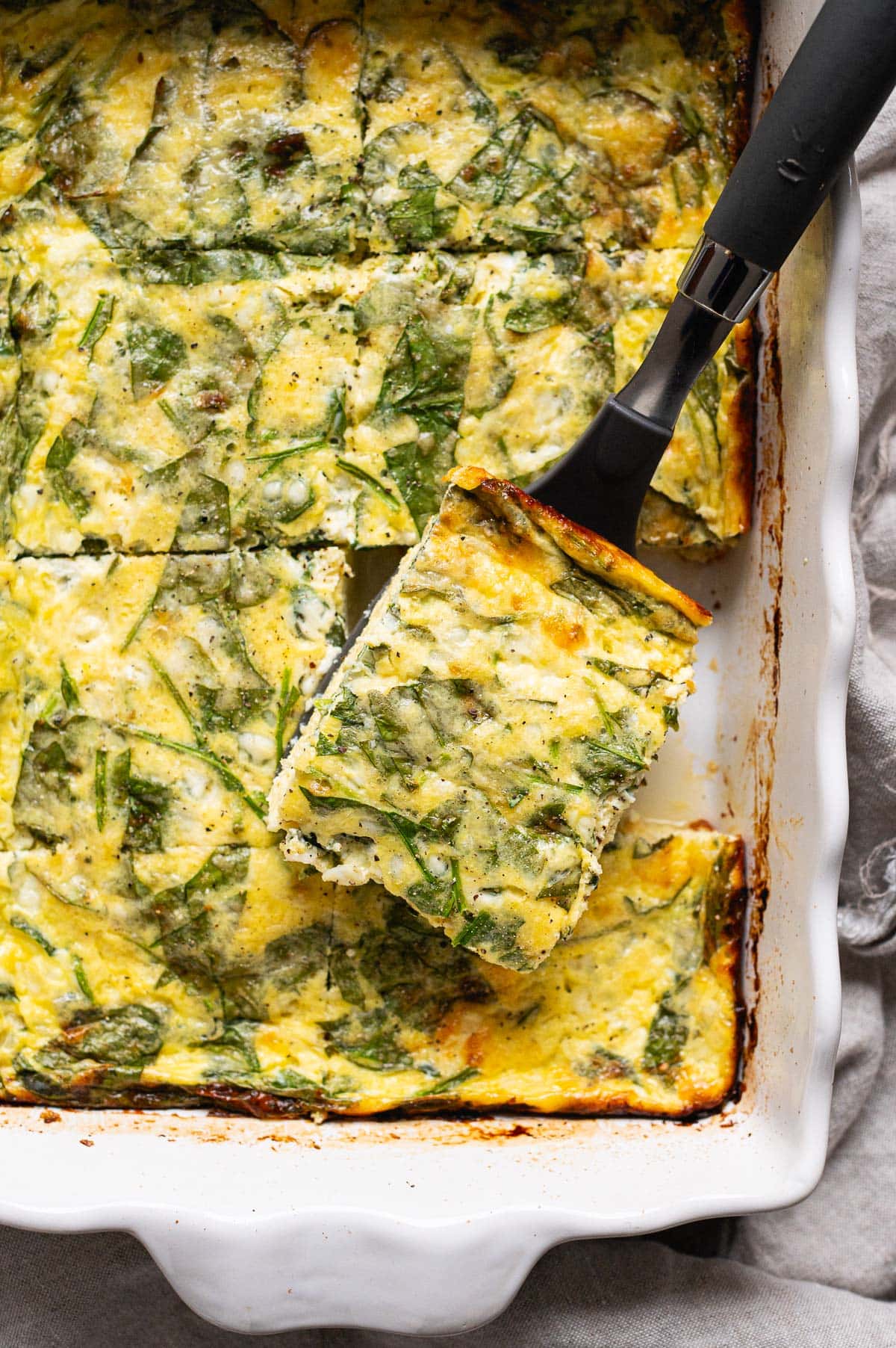 Slice of cottage cheese egg bake with spinach on a spatula.
