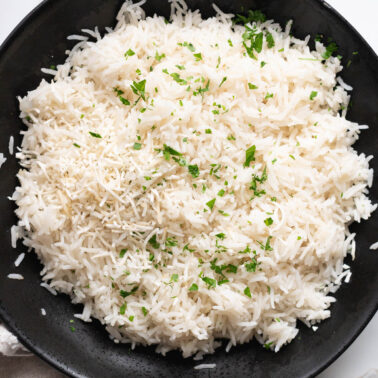 Instant pot coconut rice garnished with coconut flakes and cilantro in black bowl.