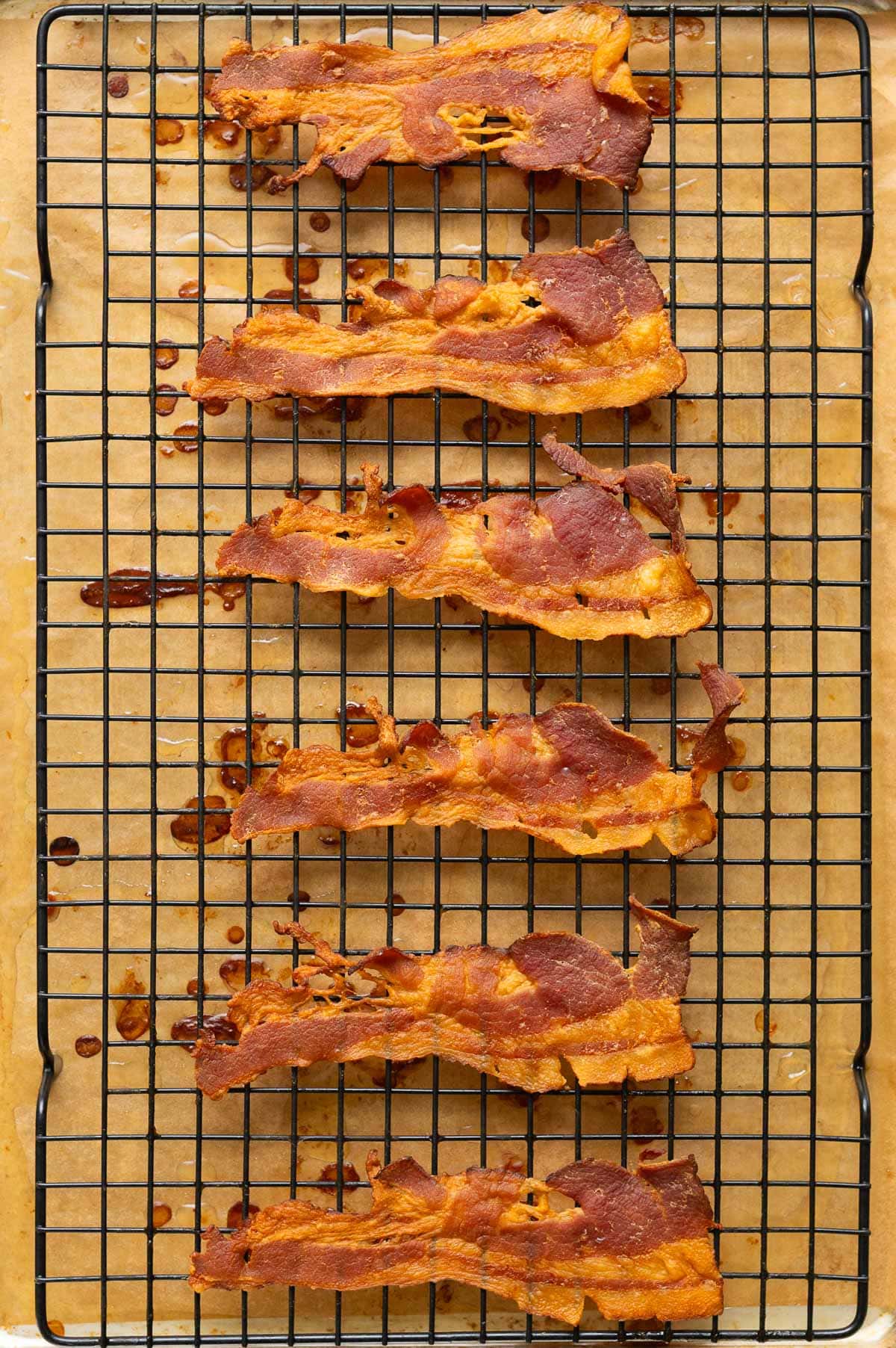 Baked bacon slices on a wire rack on top of parchment paper.