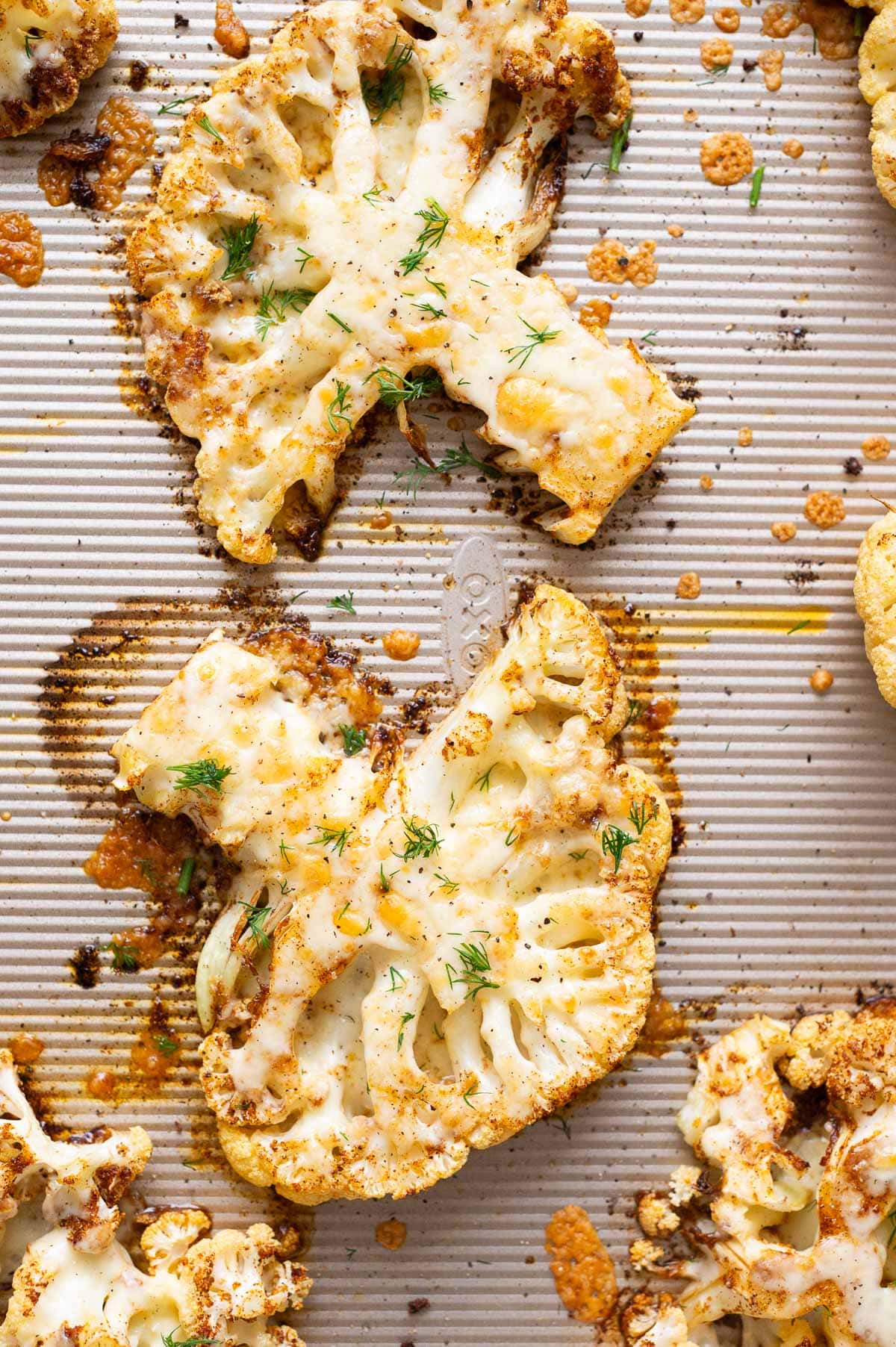 Cheesy cauliflower steaks with burnt cheese edges on a baking sheet.
