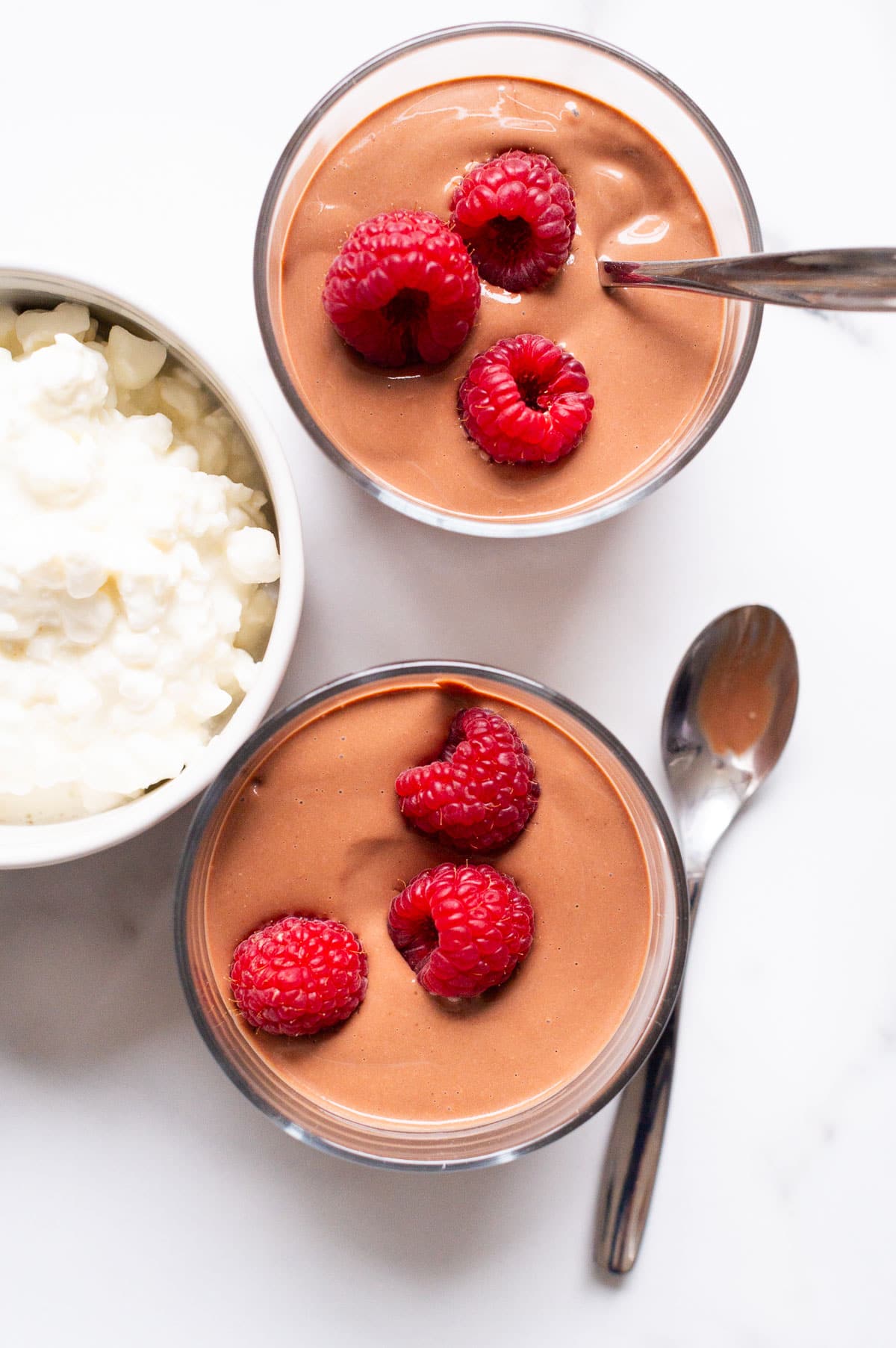 Cottage cheese chocolate pudding garnished with raspberries in small cups with spoons.
