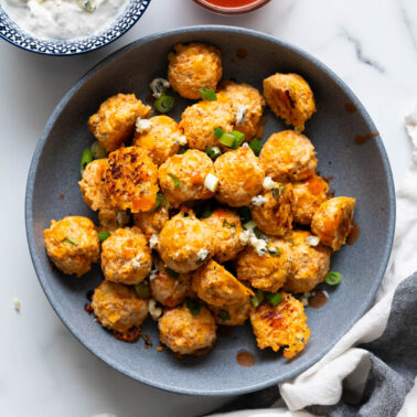 Buffalo chicken bites garnished with hot sauce, green onion and blue cheese in a bowl.