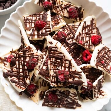Frozen cottage cheese bark with raspberries and chocolate drizzle in a bowl.