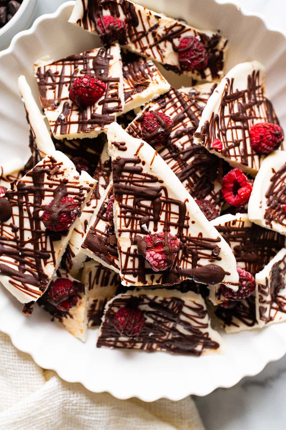 Frozen cottage cheese bark with raspberries and chocolate drizzle in a bowl.