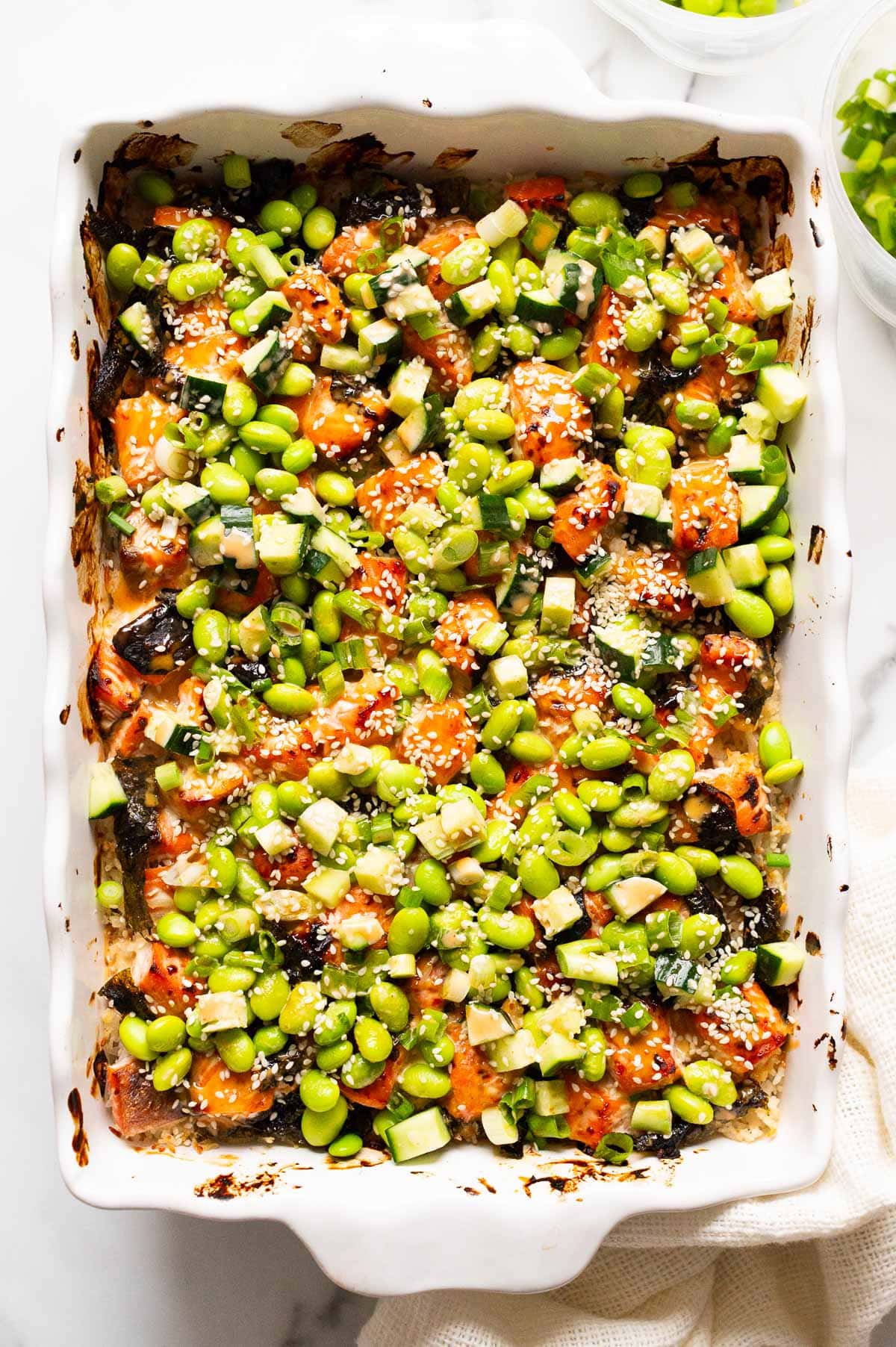 Salmon sushi bake with edamame beans, cucumber, green onion and sesame seeds in a baking dish.