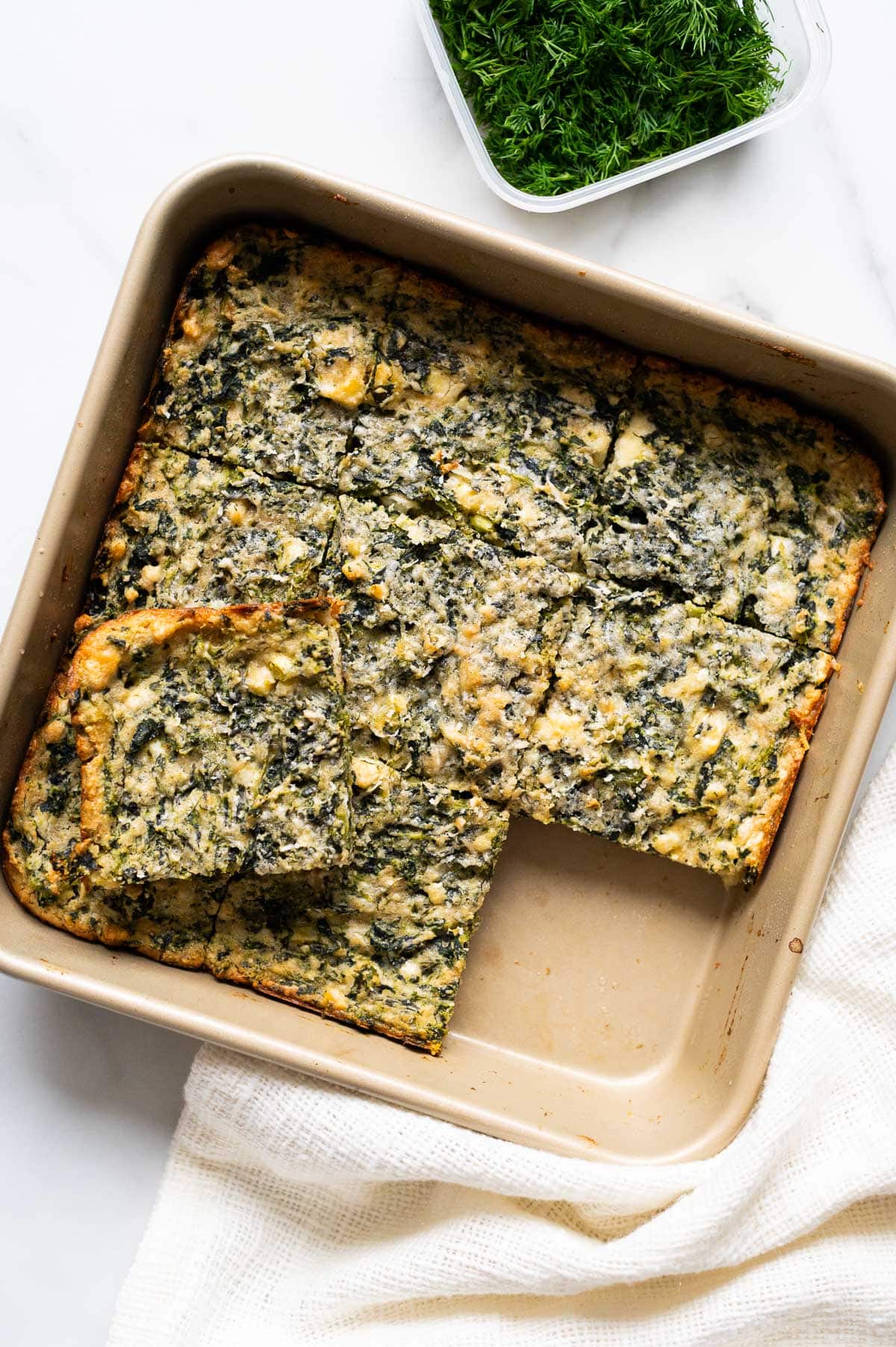 Spinach feta brownies cut into nine squares in a baking dish. One brownie removed.