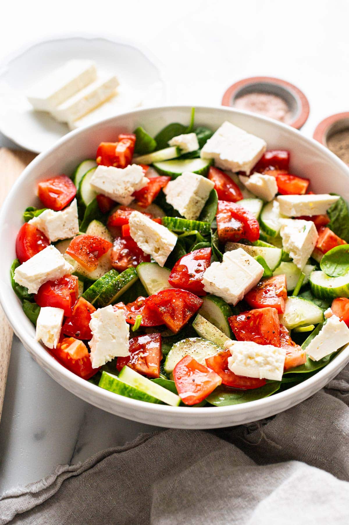 Spinach salad with cucumbers, tomatoes and feta cheese in a bowl.