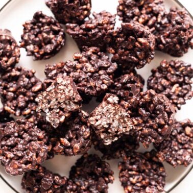 Chocolate rice krispie treats on a plate with one cut in half showing texture.