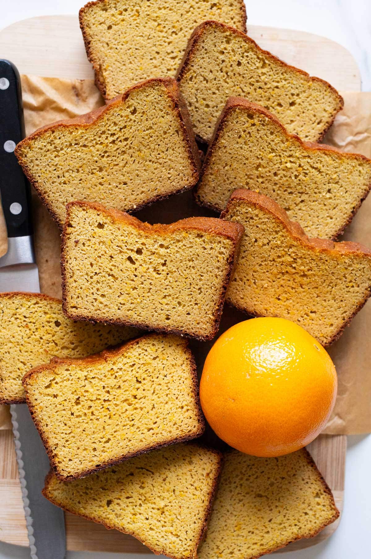 Slices of whole orange blender cake on a cutting board with whole orange and knife next to it.