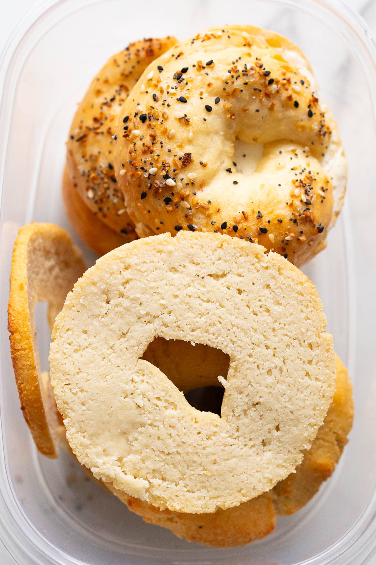 Sliced in half bagel in container with other bagels.