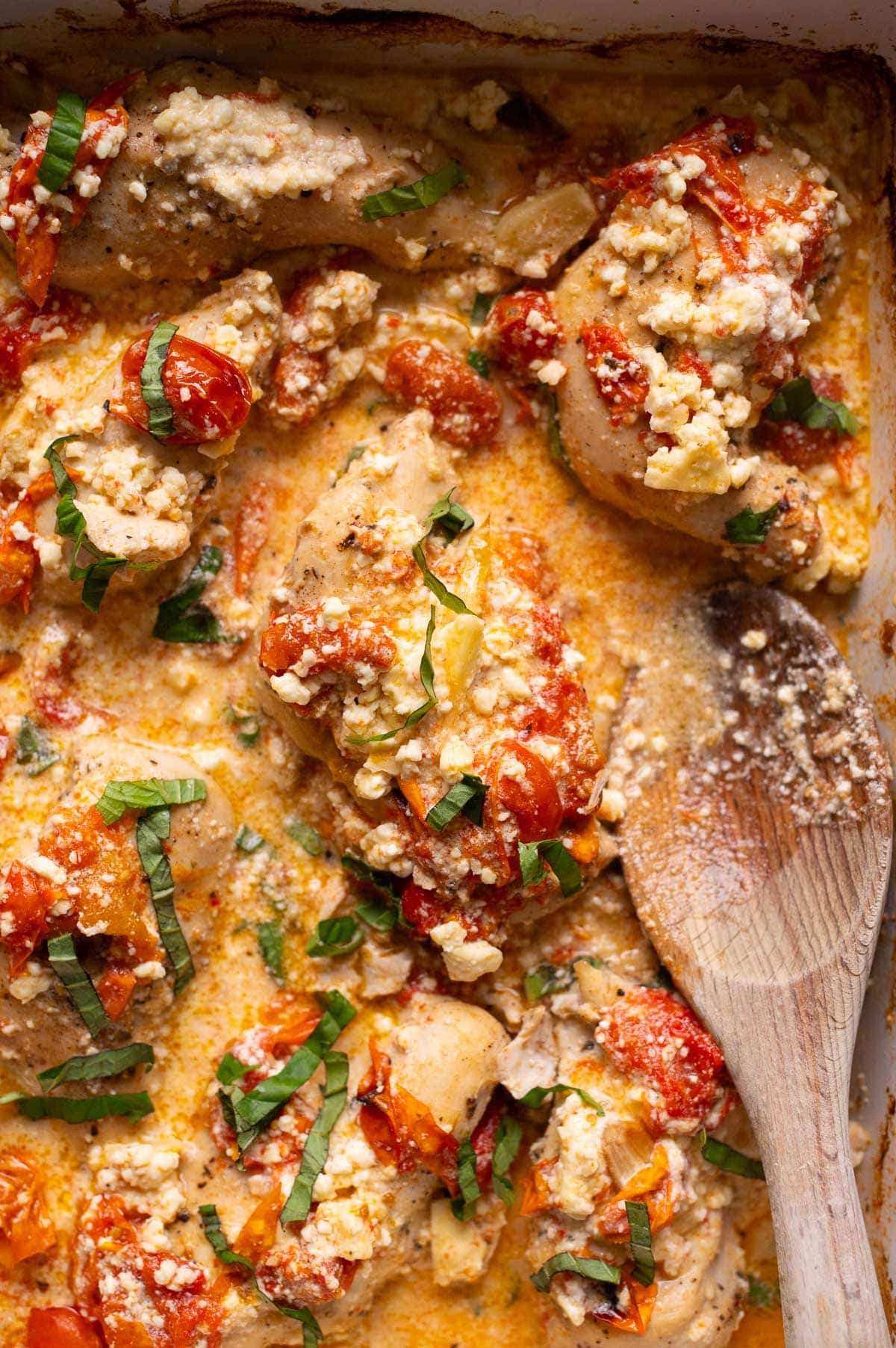 Baked feta chicken in a baking dish and wooden spoon in the sauce.