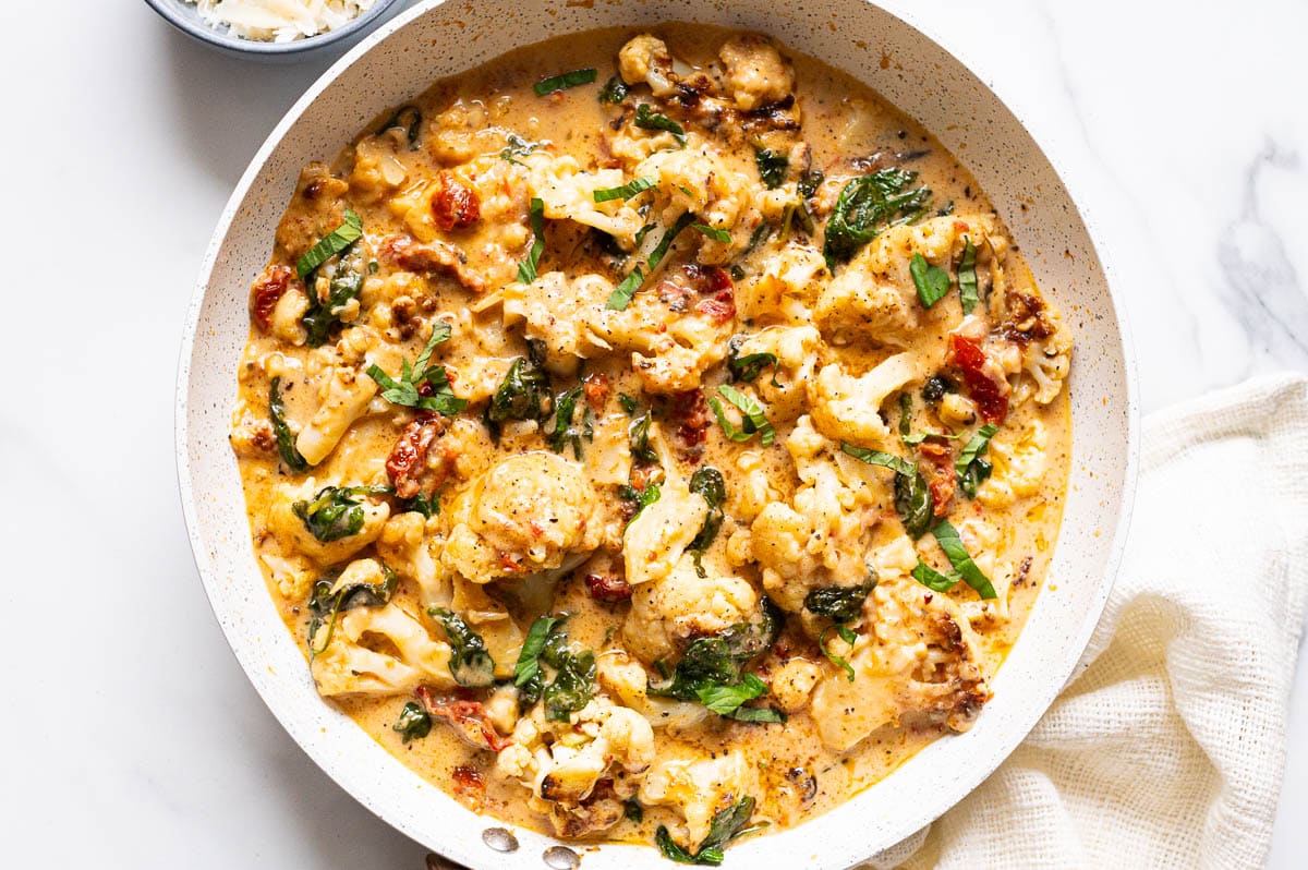 Sauteed cauliflower in creamy sauce with sun dried tomatoes and spinach in a skillet.