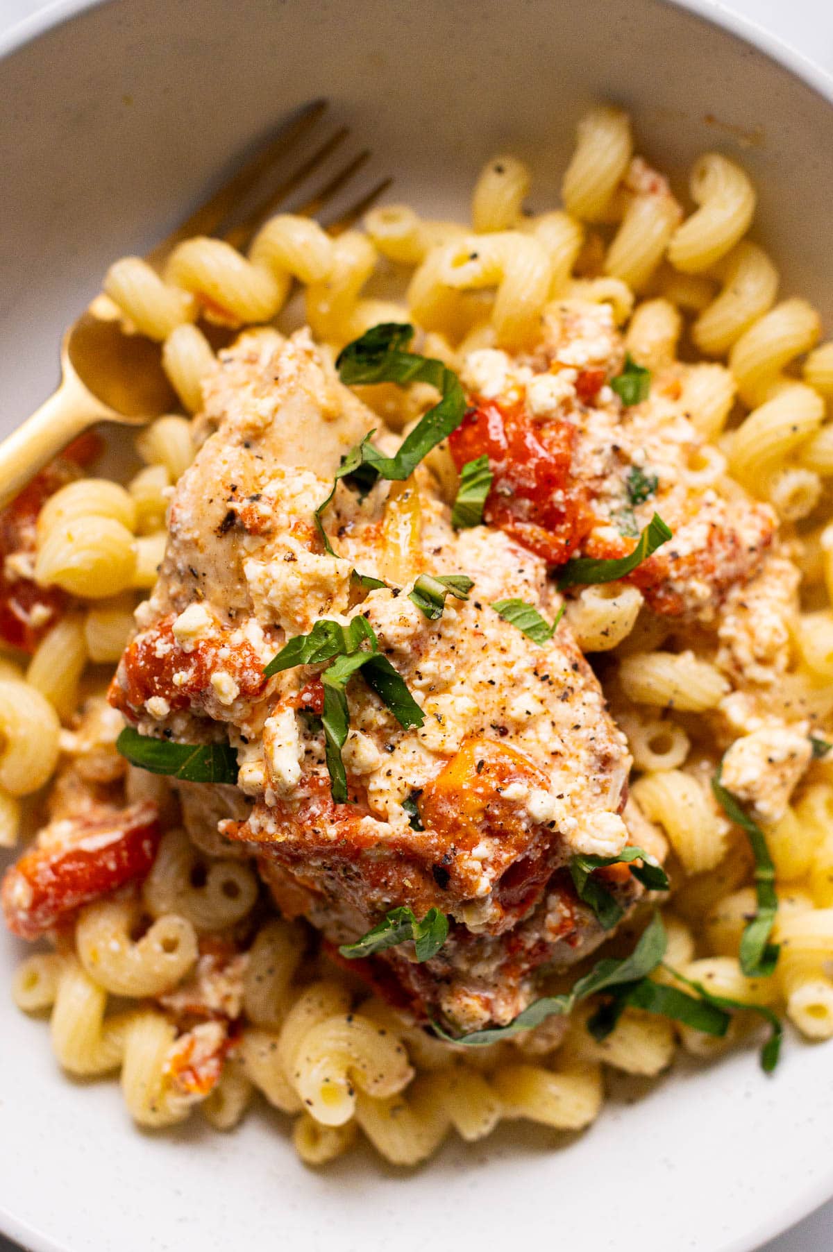 Baked feta chicken served over pasta in a bowl with a fork.
