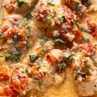 Baked feta chicken garnished with basil in a baking dish.