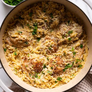 Lemon chicken orzo garnished with parsley in a Dutch oven.