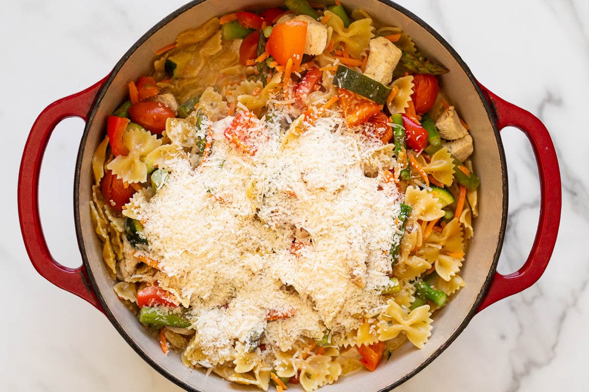 Cooked pasta primavera topped with Parmesan cheese in red pot.